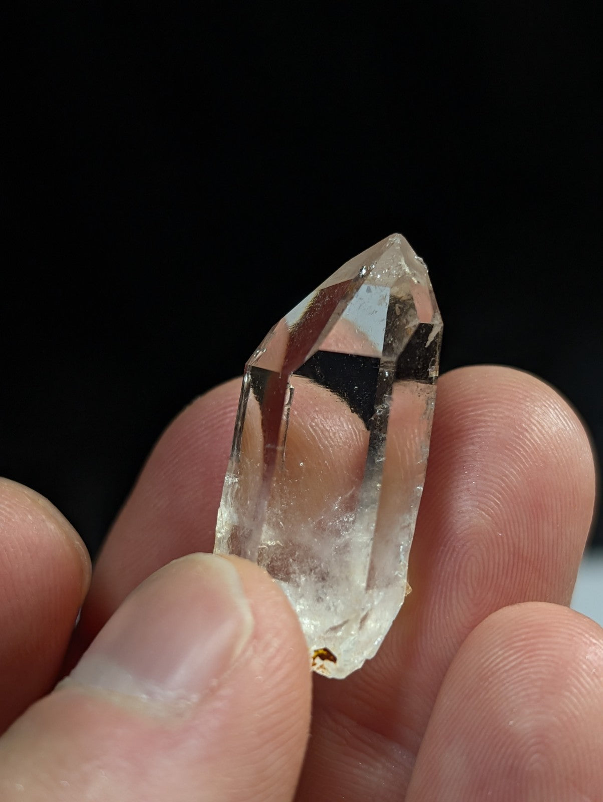 A clear, faceted quartz crystal held between fingers.