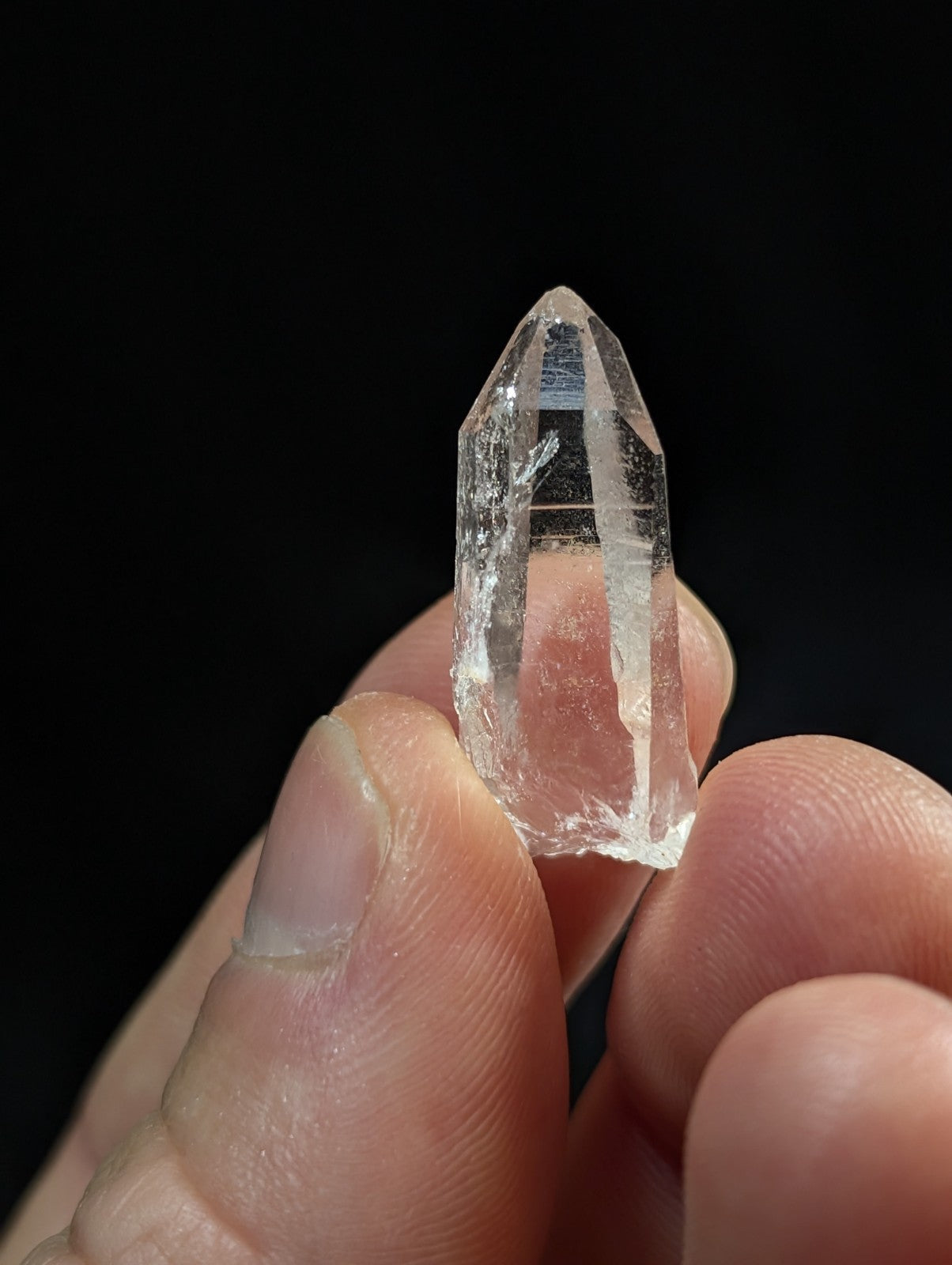 A clear, faceted quartz crystal held delicately between fingers.