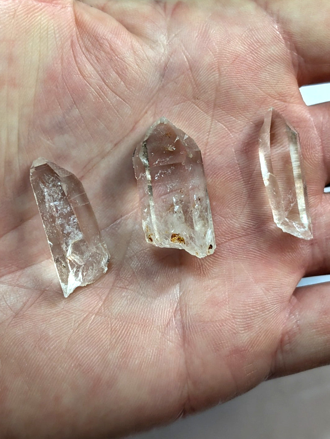 Three translucent quartz crystals with natural facets and slight imperfections, held in an open palm.