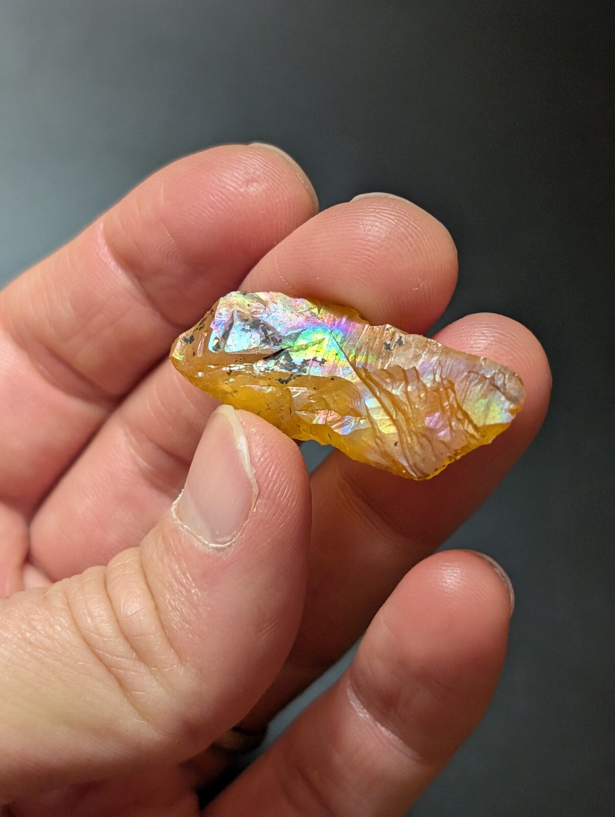 A translucent yellow-orange opal with a shimmering, iridescent surface displaying rainbow hues.