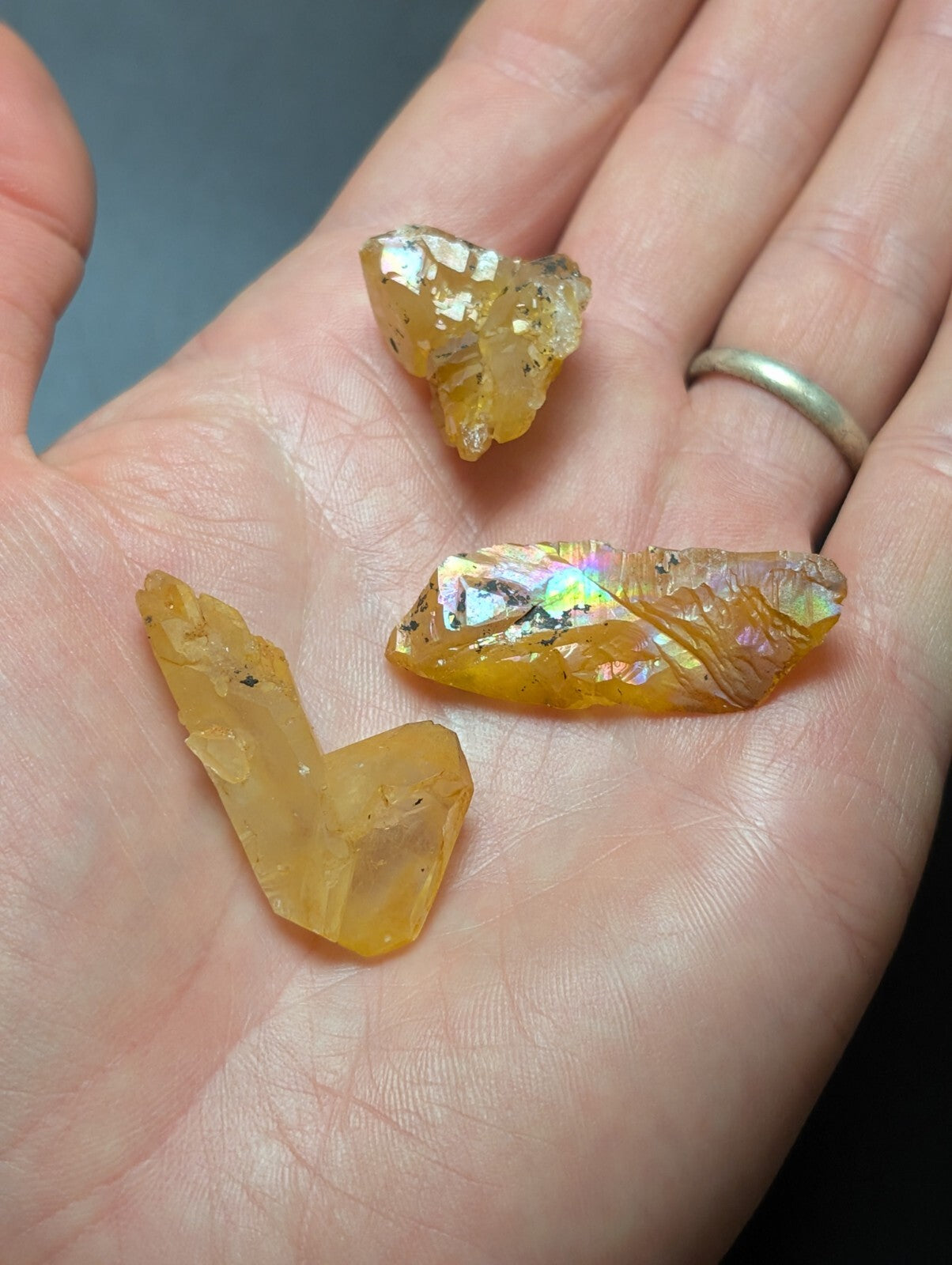 A hand holds three irregularly shaped, translucent yellow-orange crystals with iridescent flashes of rainbow hues.