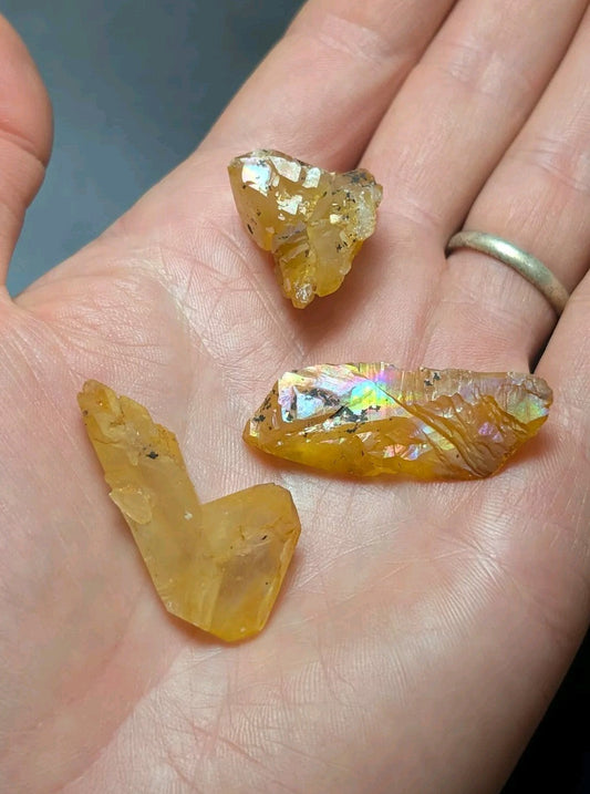 A hand holds three pieces of golden-yellow, translucent citrine crystals with iridescent flashes and natural facets.