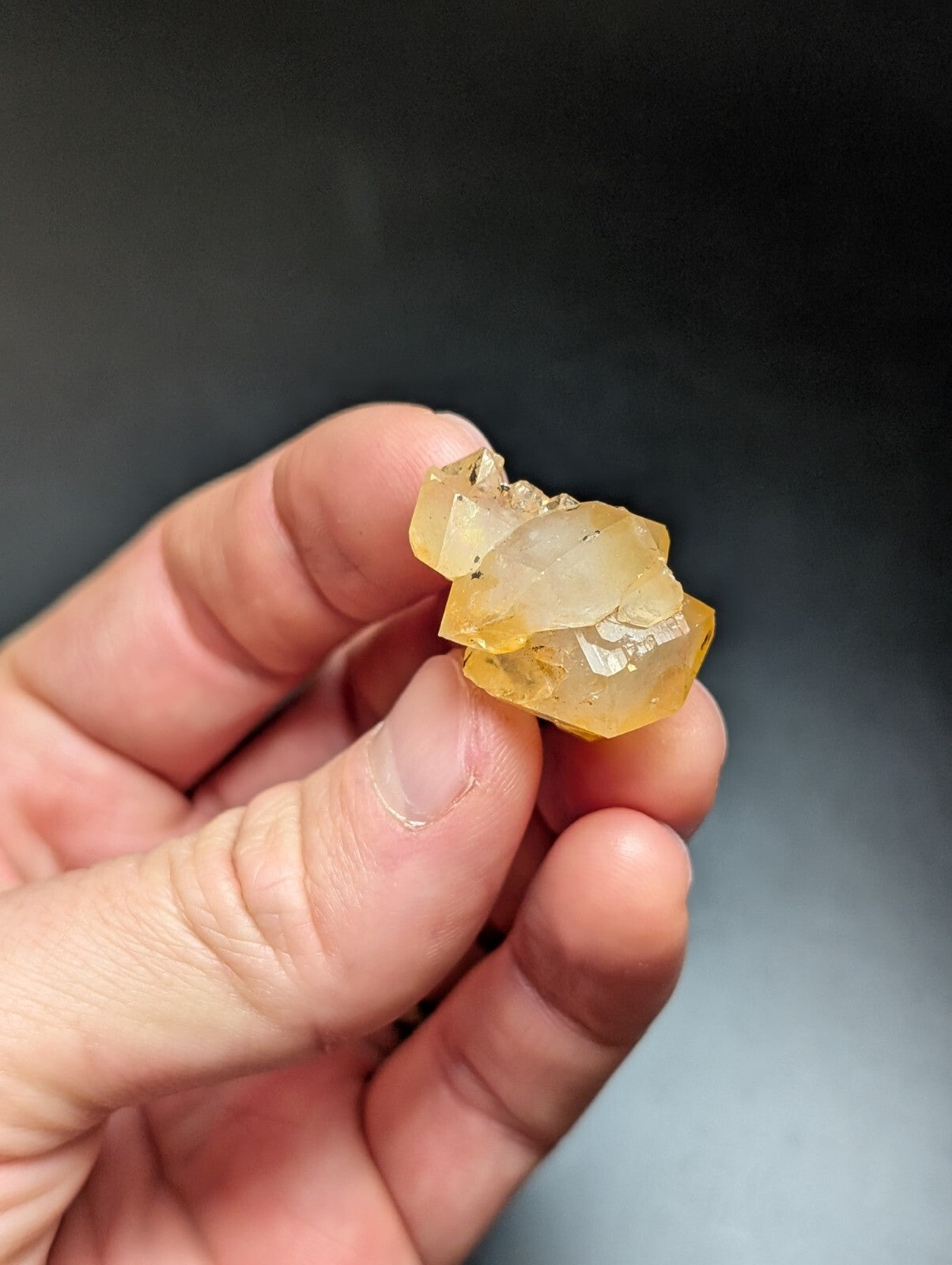 A translucent yellow-orange mineral specimen with crystalline facets, held delicately in a hand.