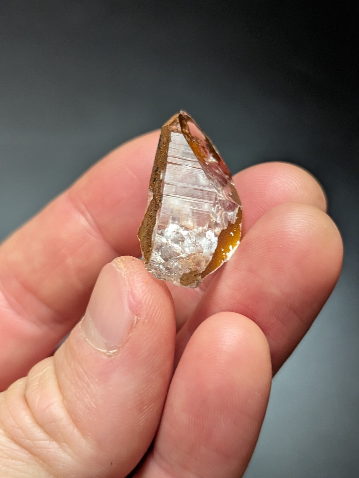 A translucent amber-hued crystal with a faceted, pointed tip and visible internal striations.