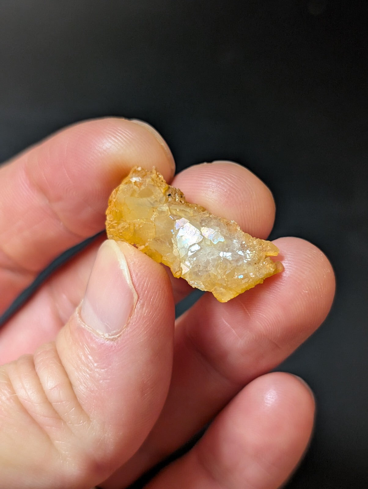 A translucent amber-colored, irregularly shaped piece of natural resin held between fingers.