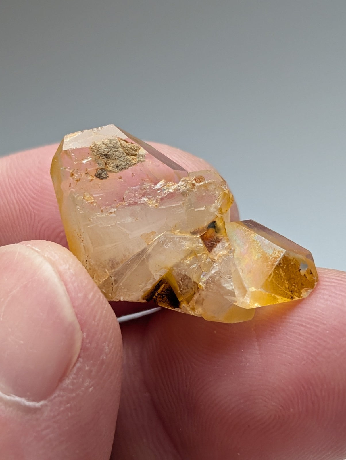 A translucent golden-yellow Arkansas quartz crystal with natural iridescence and mineral inclusions held between fingers
