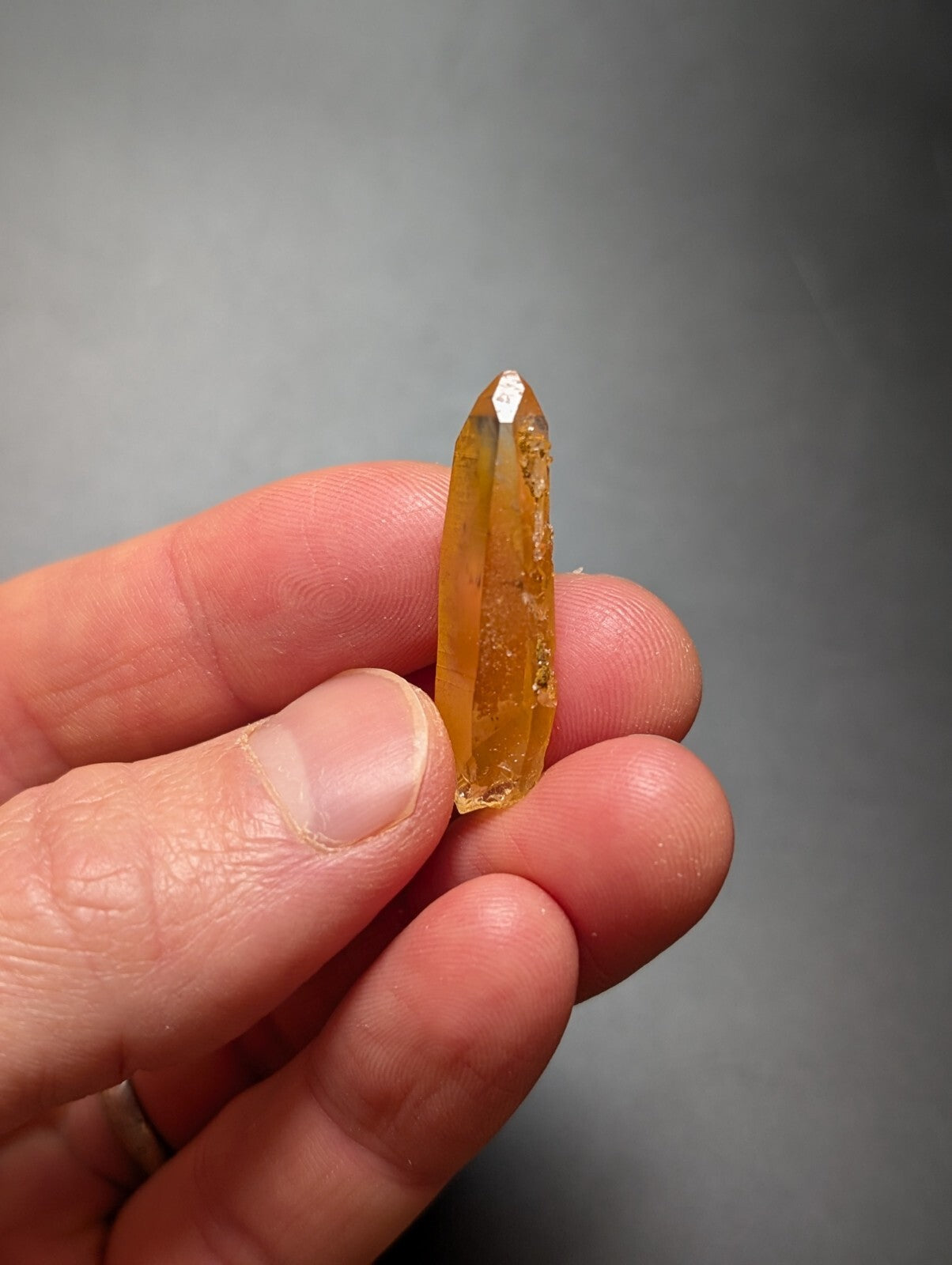 A translucent golden-yellow citrine crystal with a pointed tip and natural facets, held delicately between fingers.