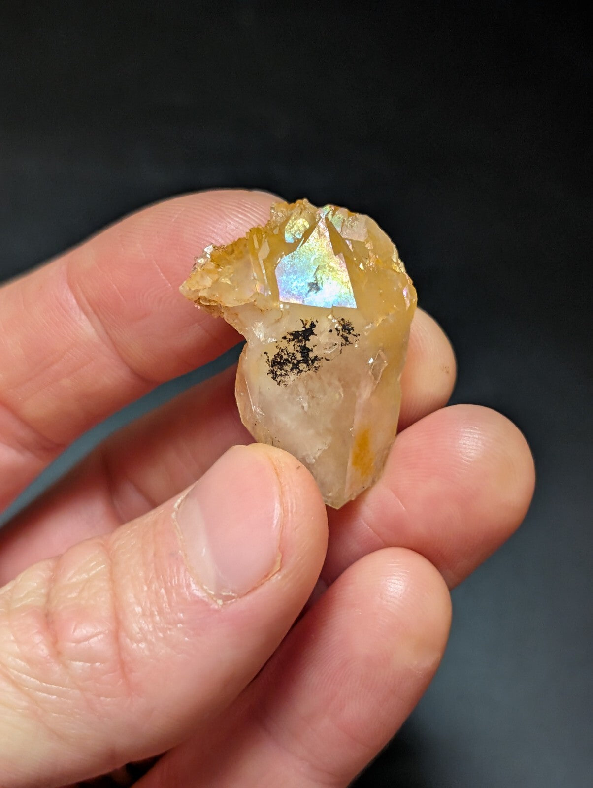 A translucent amber-colored crystal with a faceted, iridescent surface and dark inclusions.
