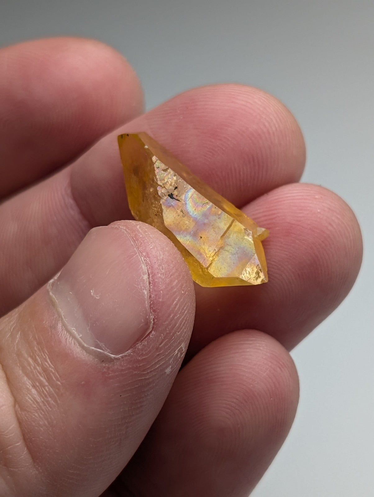 A translucent golden yellow Arkansas quartz crystal with faceted geometric shape and natural iridescent flashes
