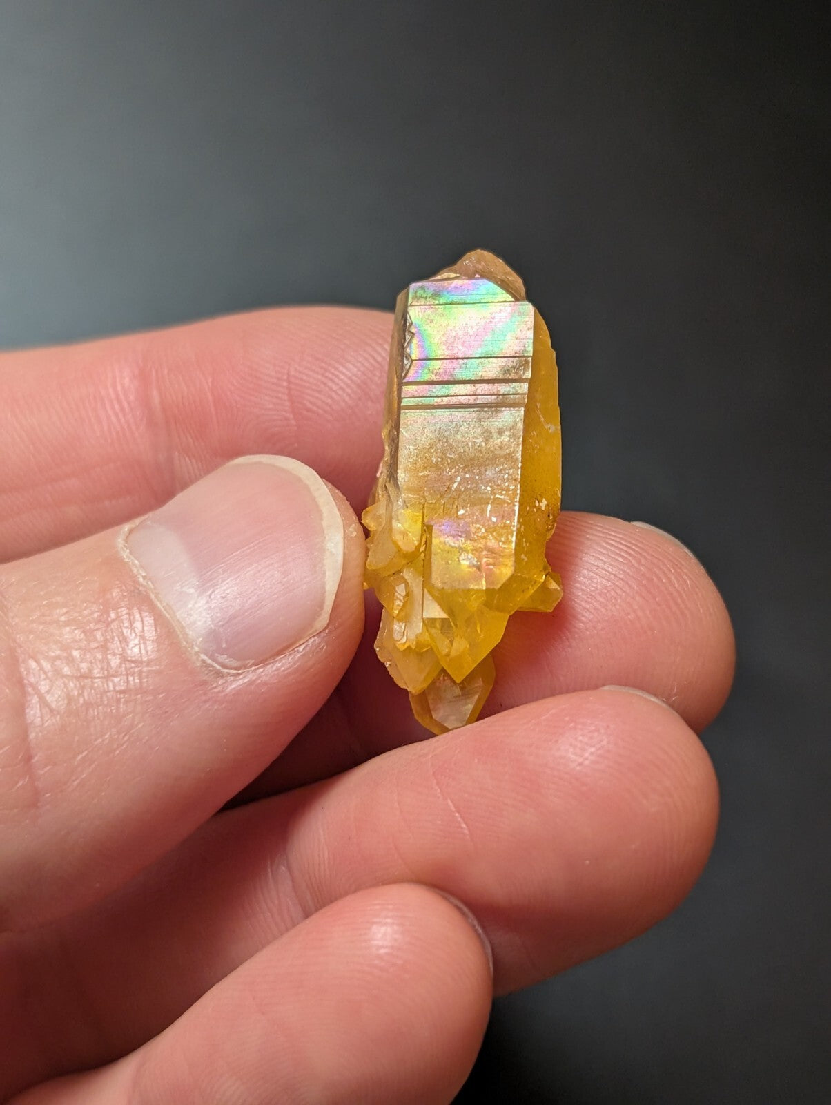 A translucent golden-yellow crystal with a faceted, iridescent top and rougher, jagged lower sections.