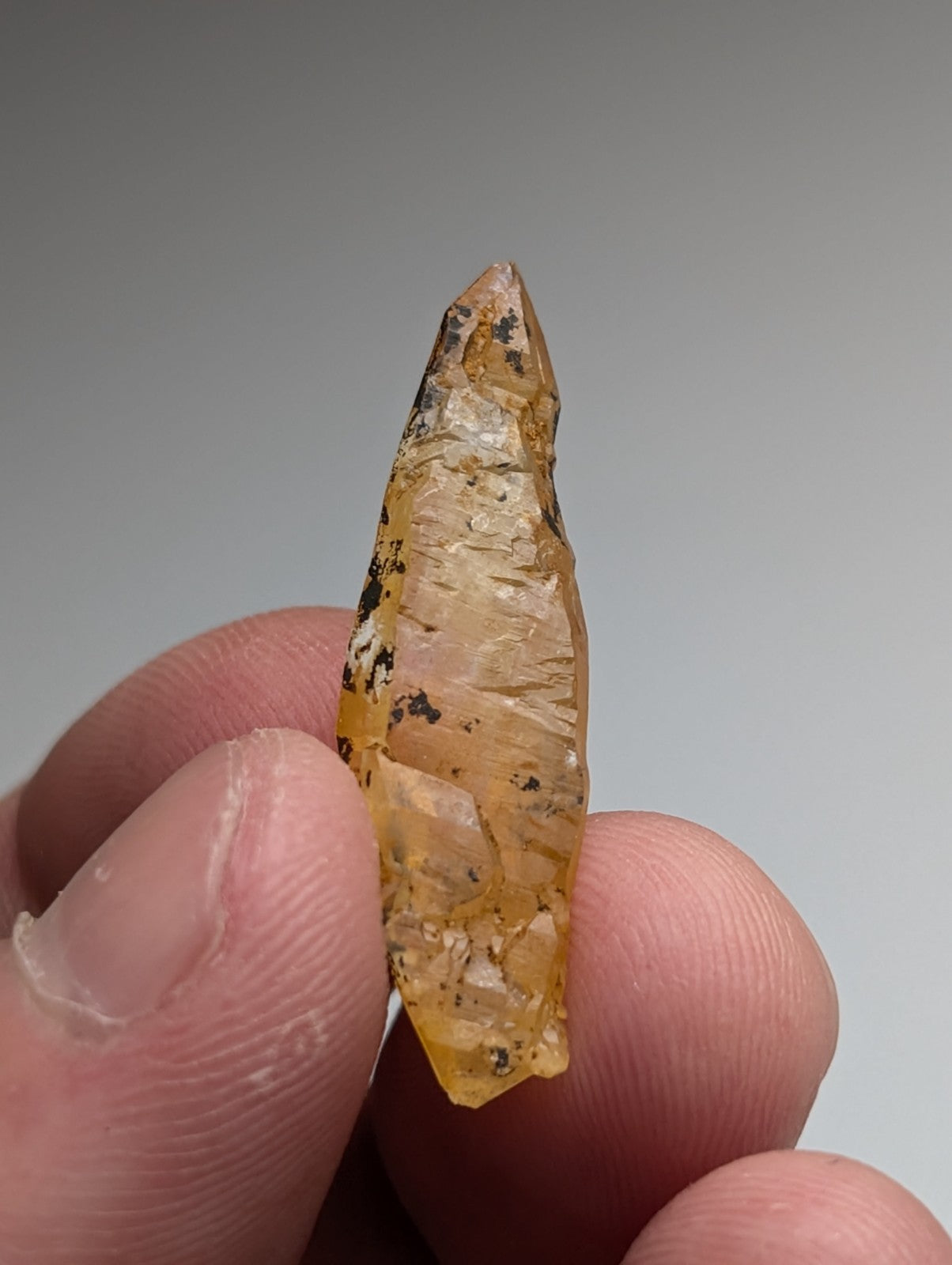 A translucent amber arkansas quartz crystal with dark inclusions and pointed tip held between fingers in a set of three