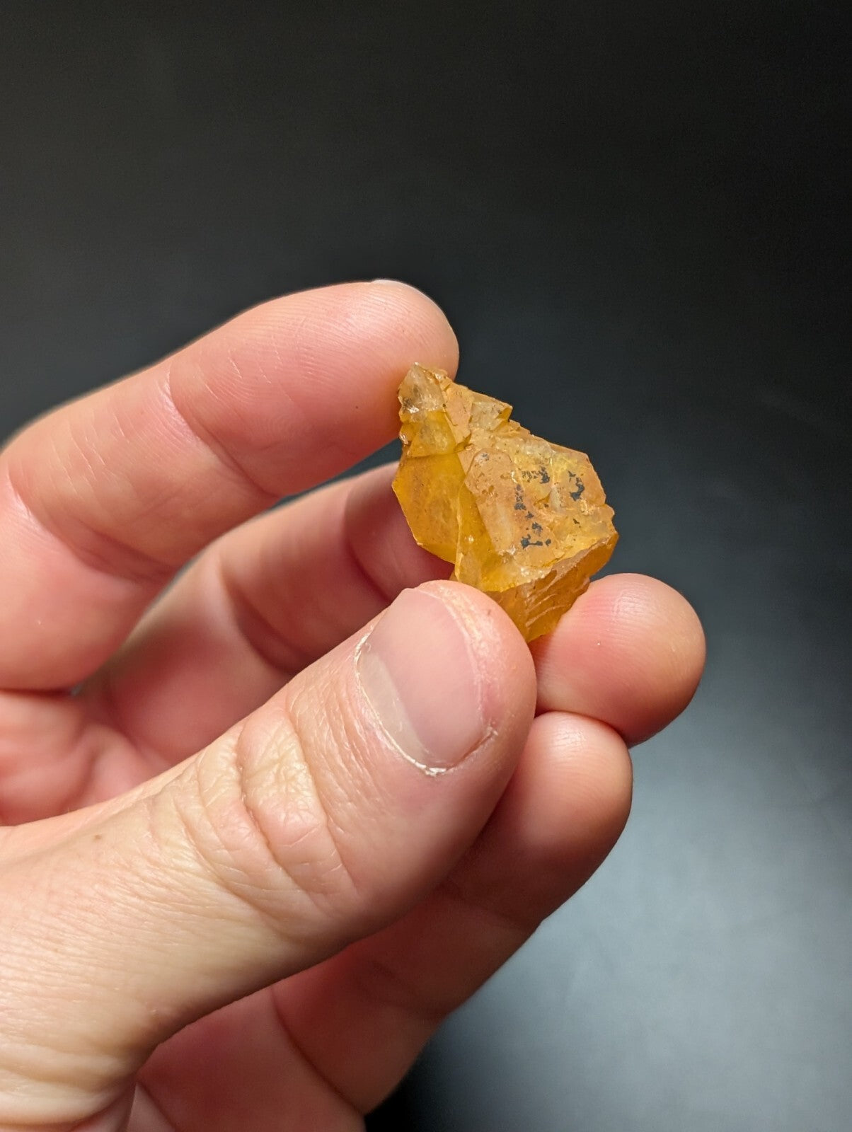 A translucent amber-colored mineral specimen with a rough, faceted surface and small dark inclusions.