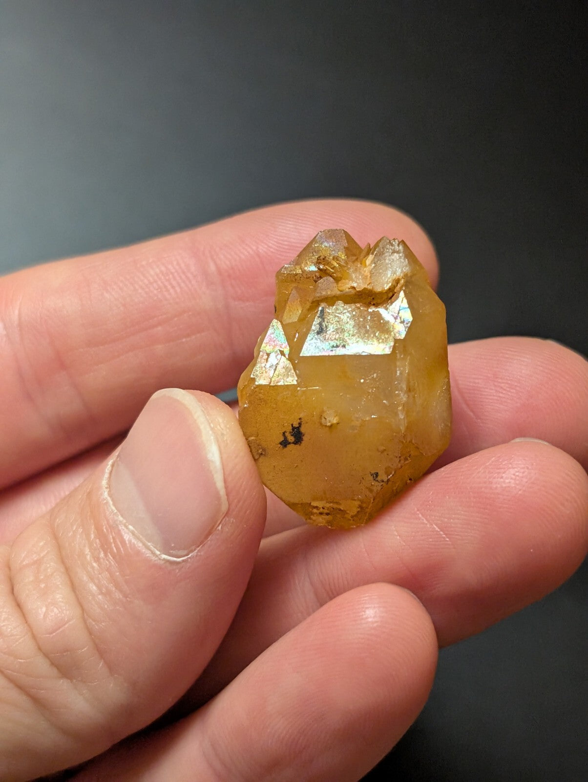 A translucent amber-colored crystal with a faceted, geometric shape and subtle metallic inclusions.