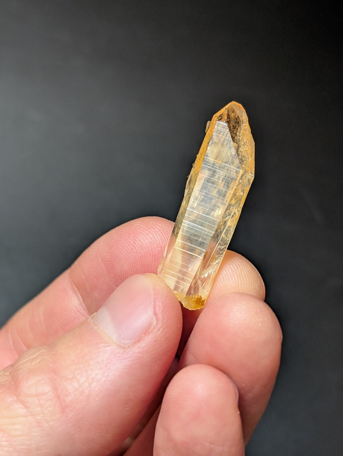 A translucent yellow crystal with a pointed tip and visible internal striations, held gently between fingers.