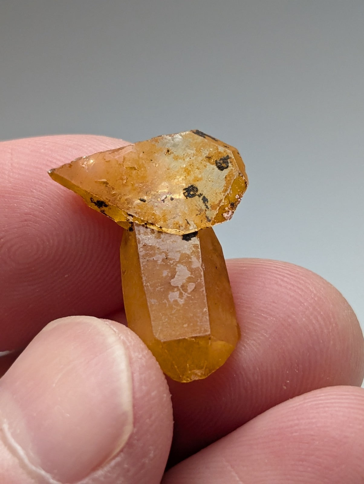 A translucent amber-colored arkansas quartz crystal shaped like a faceted mushroom with dark inclusions and natural iridescence