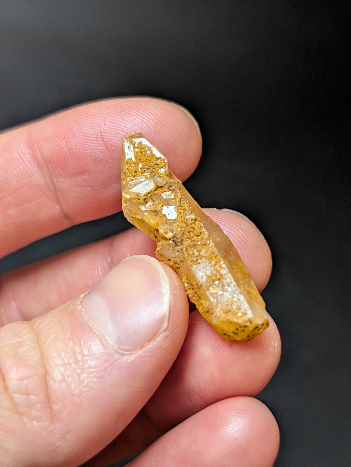 A translucent golden-yellow crystal with a pointed tip and speckled surface, held gently between fingers.