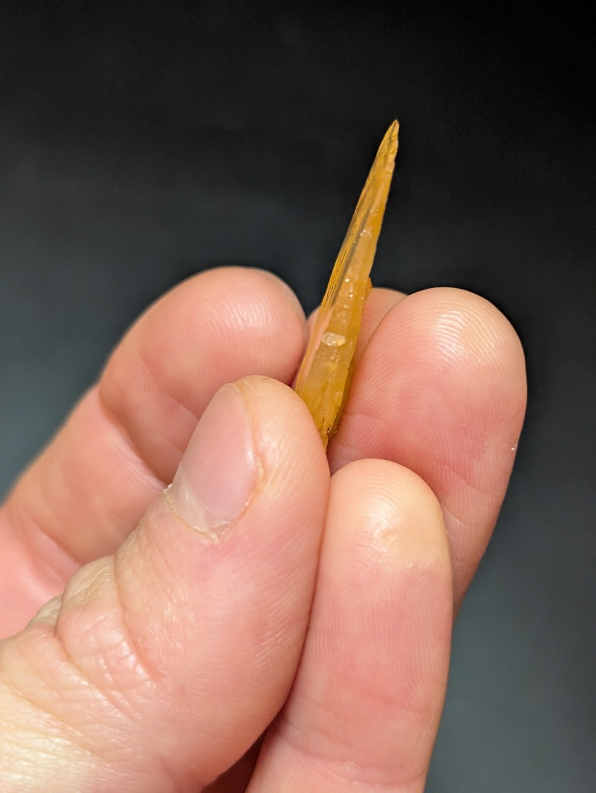 A translucent amber-colored, sharply pointed stone tool held between fingers.