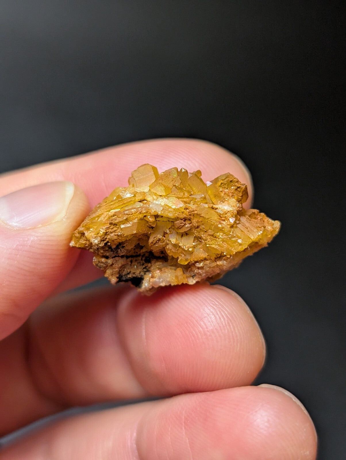 A cluster of translucent golden-yellow crystals with a rough, earthy base held gently in fingers.