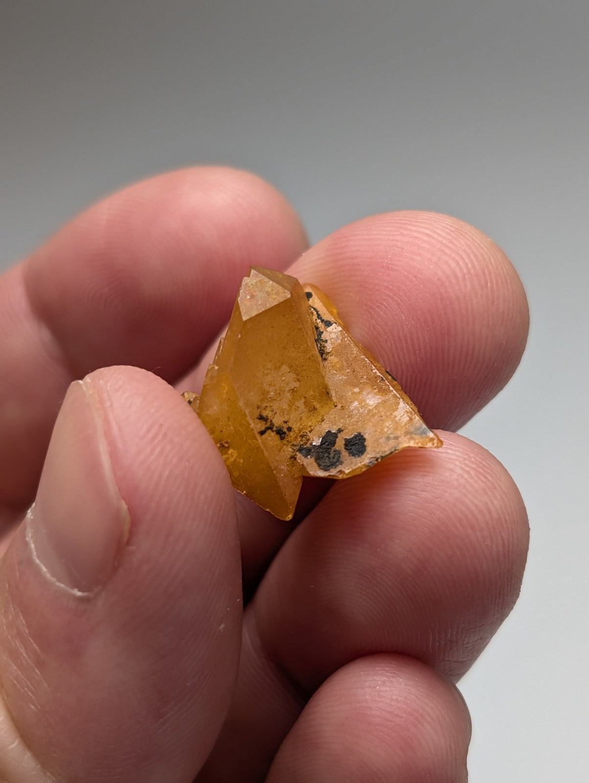 A translucent amber-colored arkansas quartz crystal with angular facets and dark inclusions held between fingers