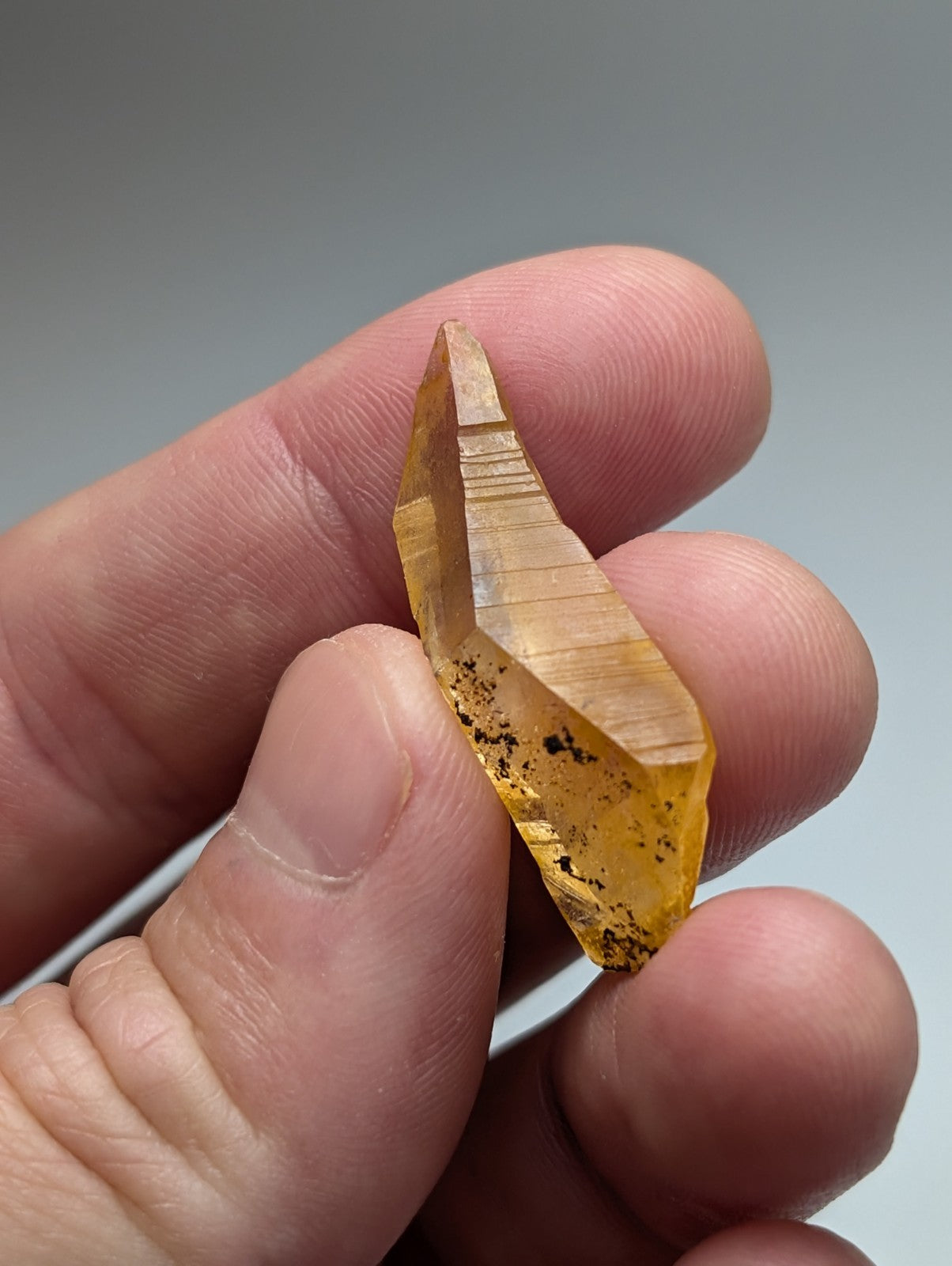 A translucent golden-yellow Arkansas quartz crystal with natural iridescence held gently between fingers
