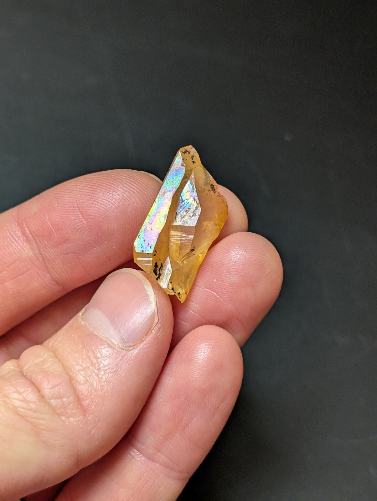 A translucent golden-yellow crystal with iridescent facets, held gently in a person’s hand.