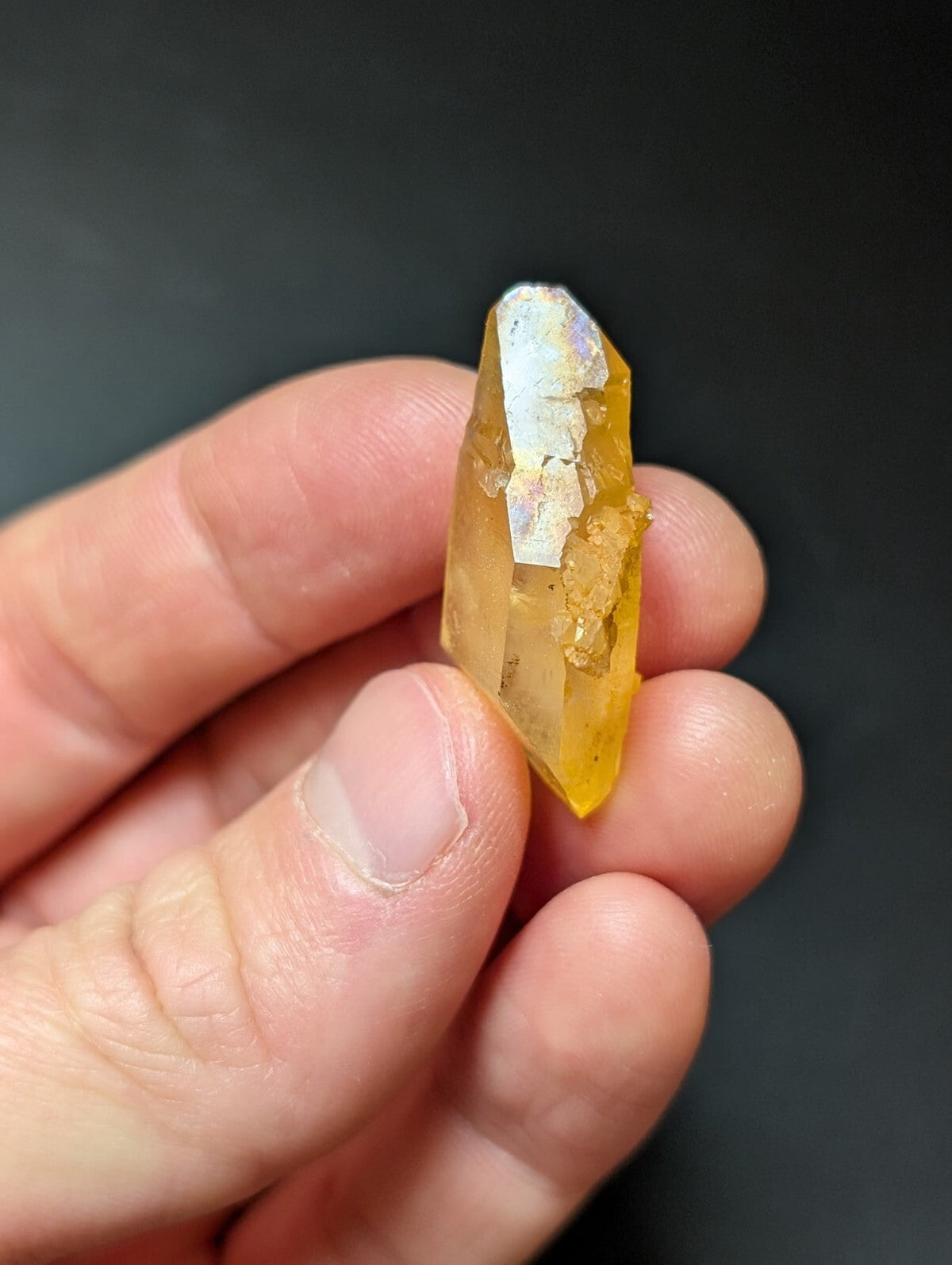 A translucent golden-yellow crystal with a pointed tip and white mineral inclusions, held gently between fingers.