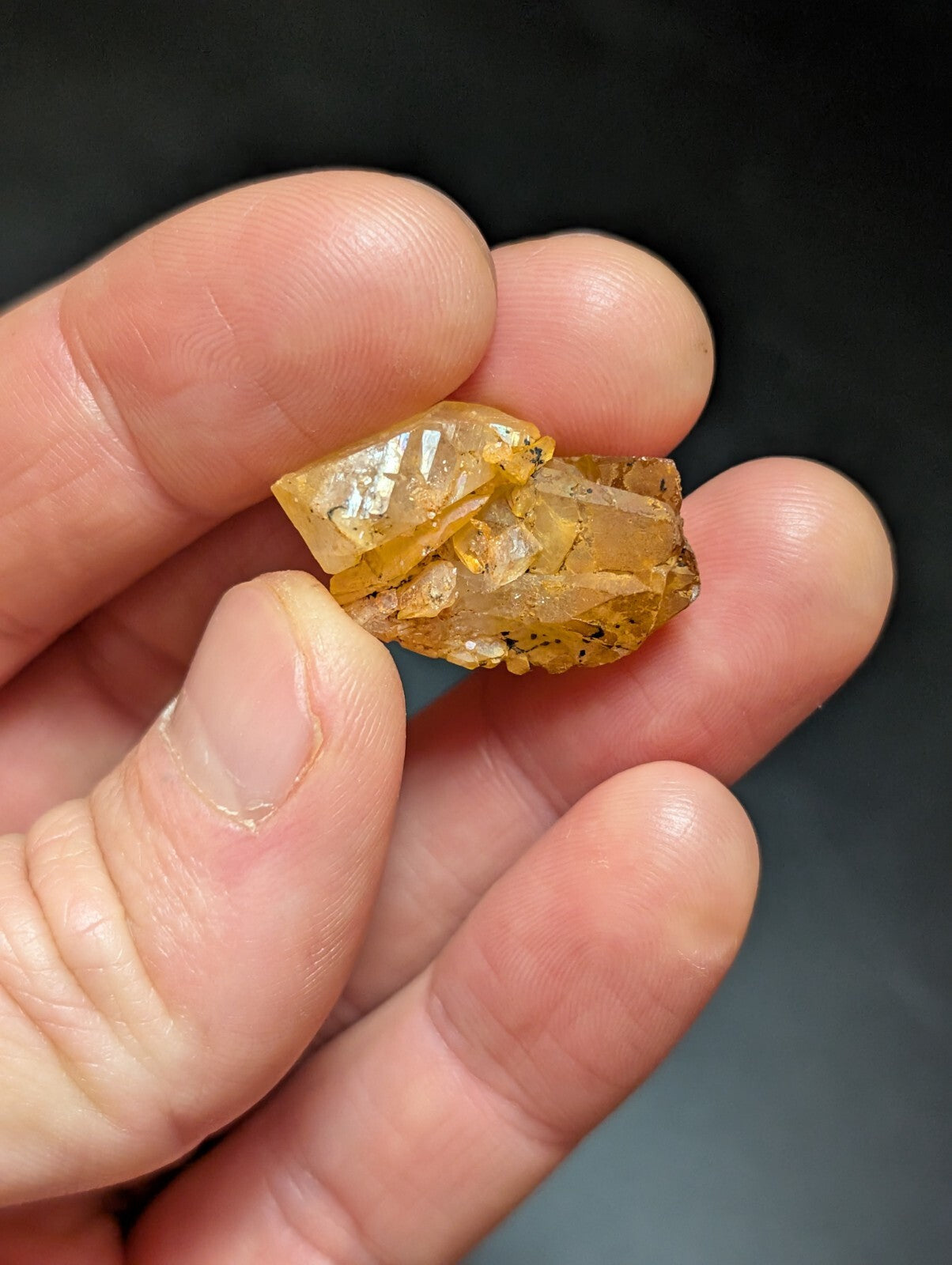A translucent amber-colored mineral specimen with visible crystalline facets and minor dark inclusions, held gently between fingers.