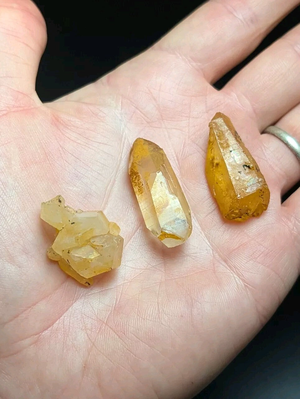 Three amber-hued crystal specimens with varying facets and natural inclusions, resting gently on an open palm.