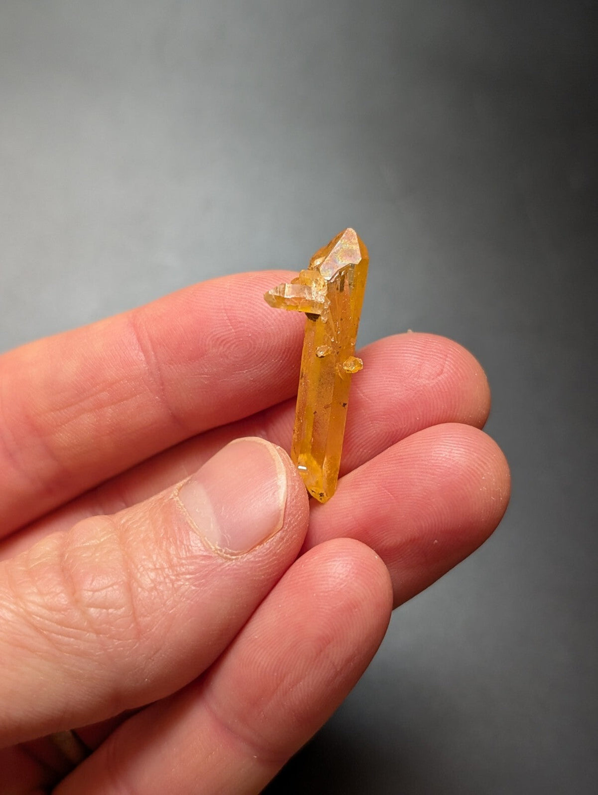 A translucent golden-yellow crystal with a pointed tip and natural facets, held gently in someone’s hand.