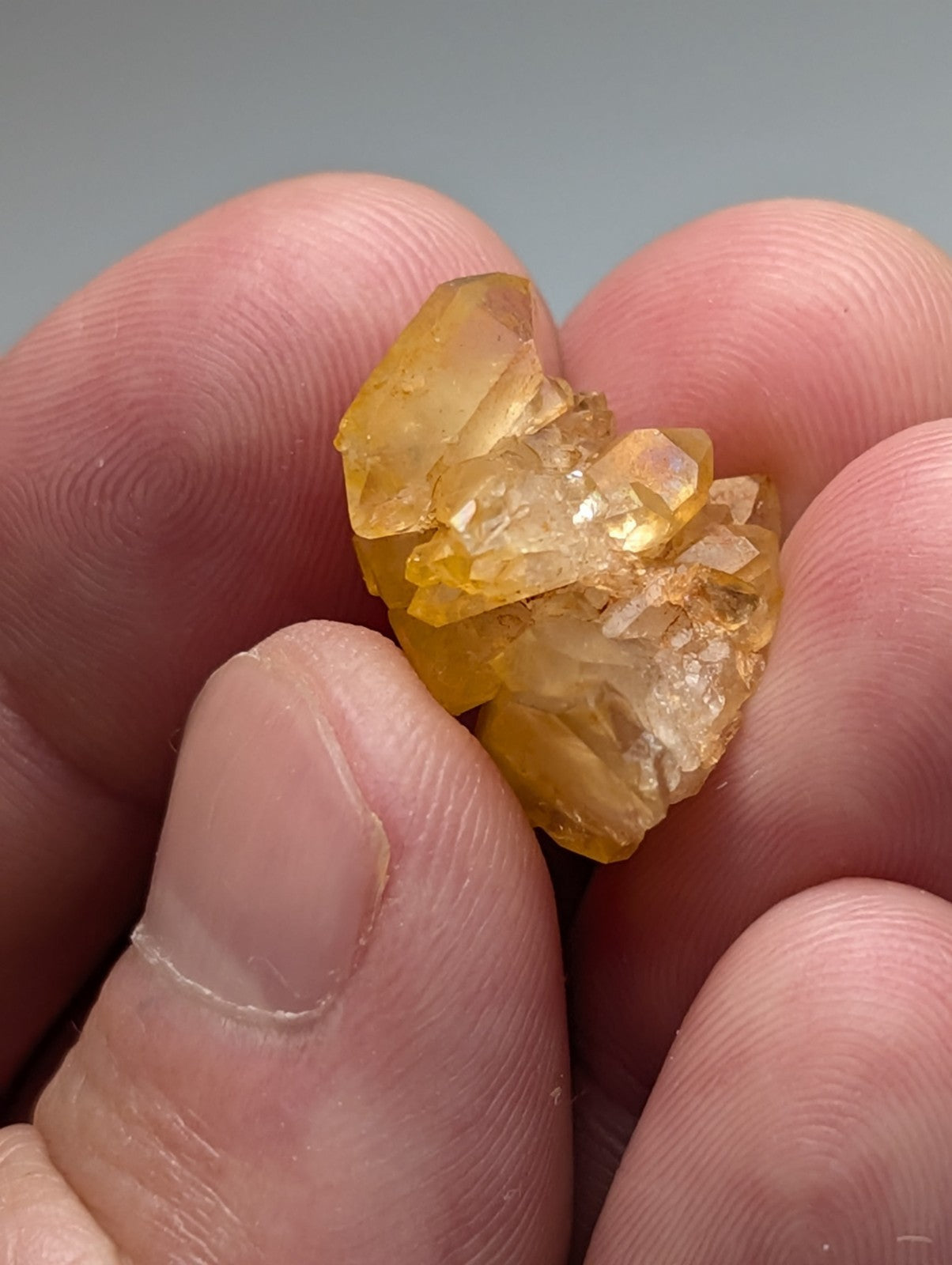 A set of 3 translucent yellow arkansas quartz crystals with natural iridescence held in a person’s fingers