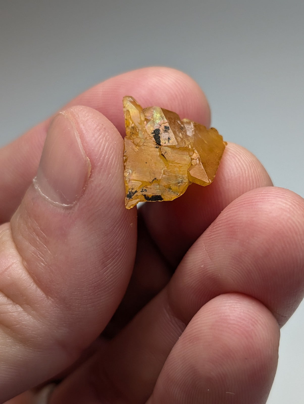 A translucent amber arkansas quartz crystal with natural iridescence and dark inclusions held between fingers