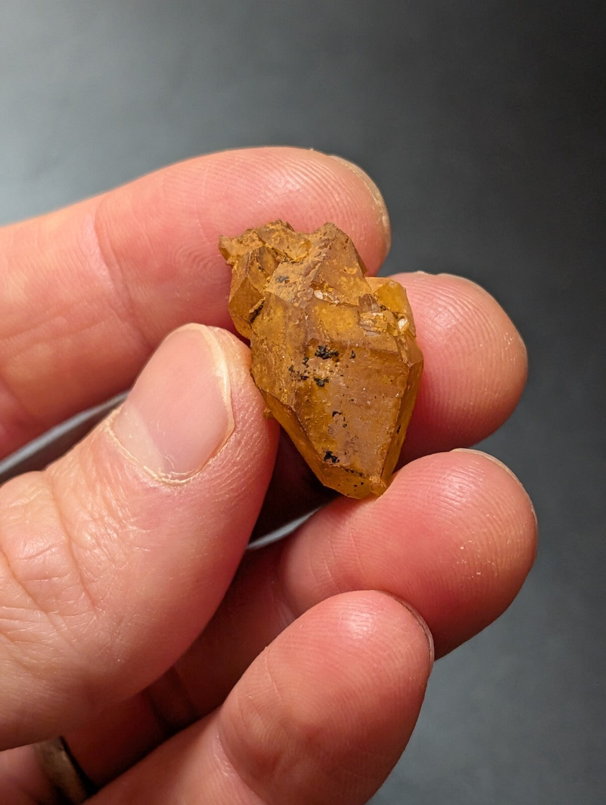 A translucent amber-colored crystal with a rough, jagged surface and small dark inclusions.