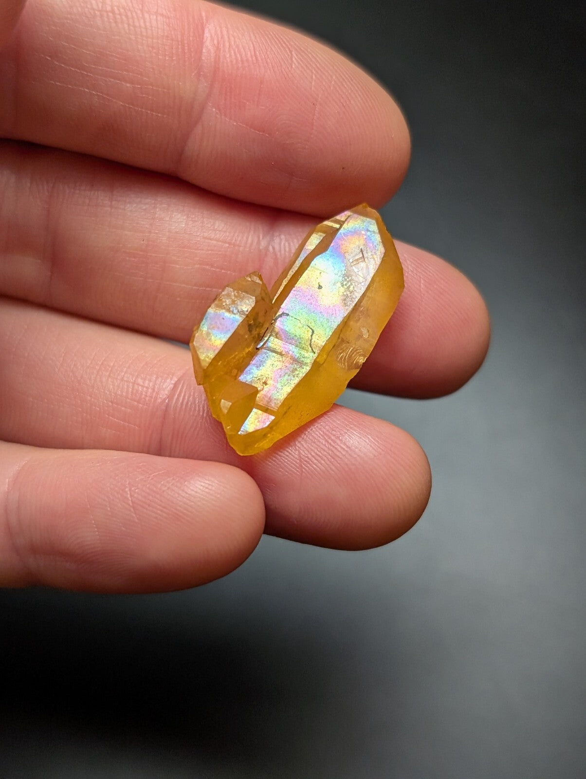A translucent golden-yellow crystal with iridescent facets, held gently in a hand.