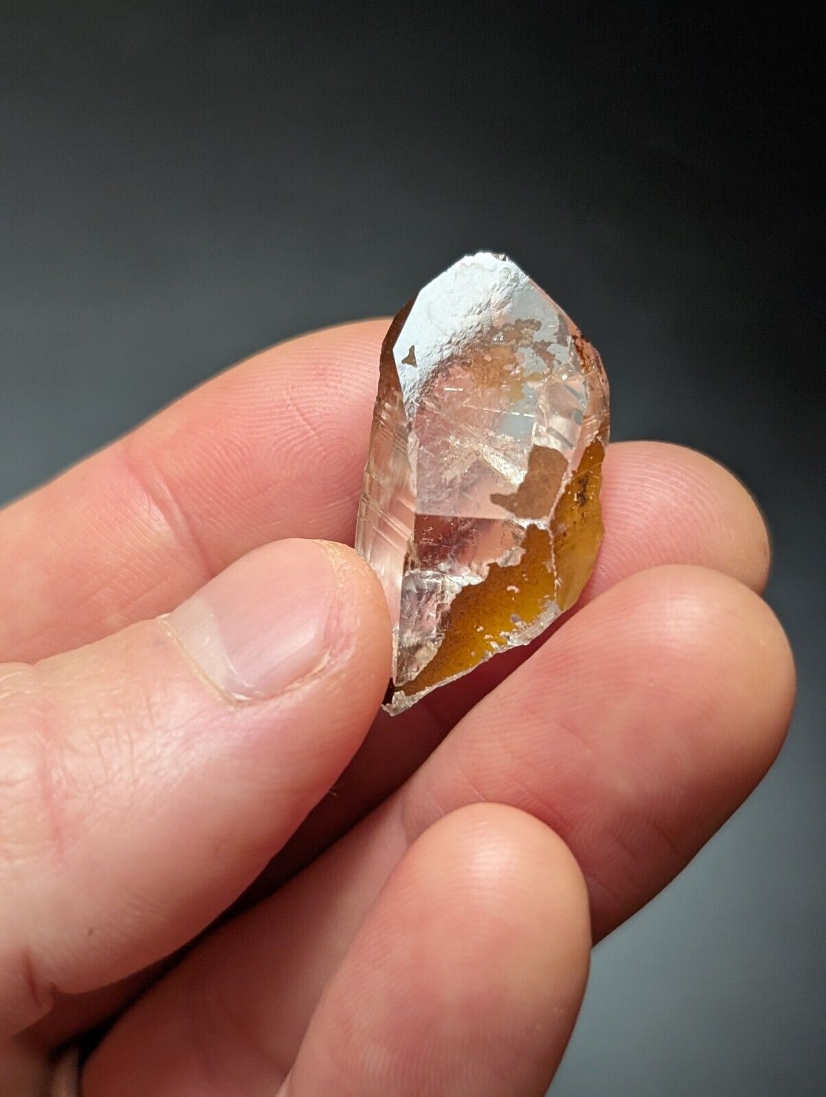Hand holding a clear and amber-colored crystal.