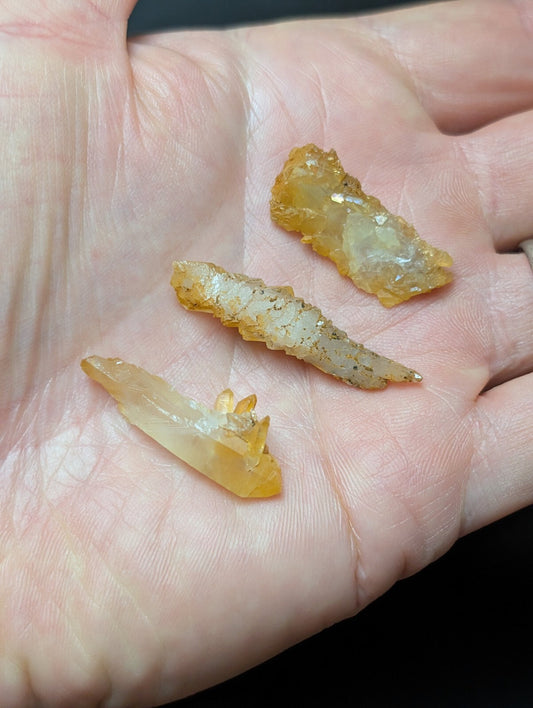 Three translucent yellow-orange crystal points with natural, jagged edges rest in an open palm.