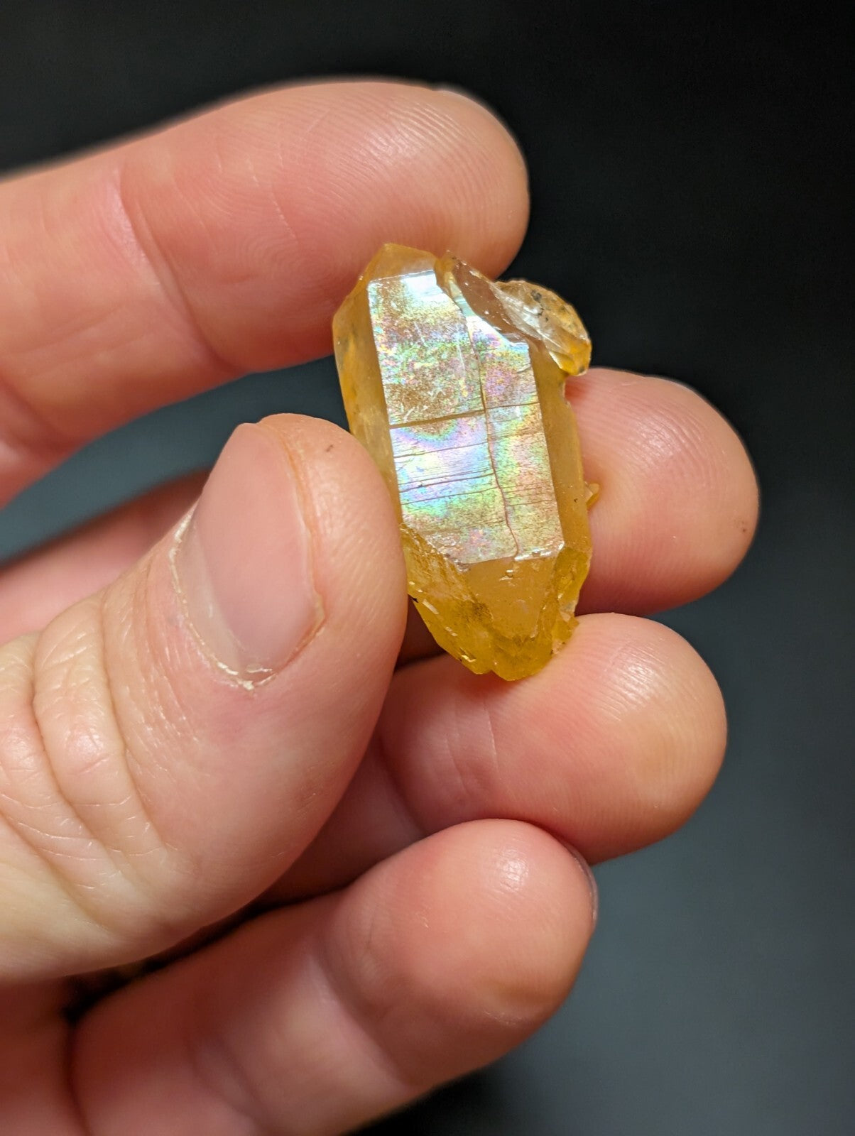 A translucent golden-yellow crystal with a faceted, prism-like structure and iridescent internal reflections.