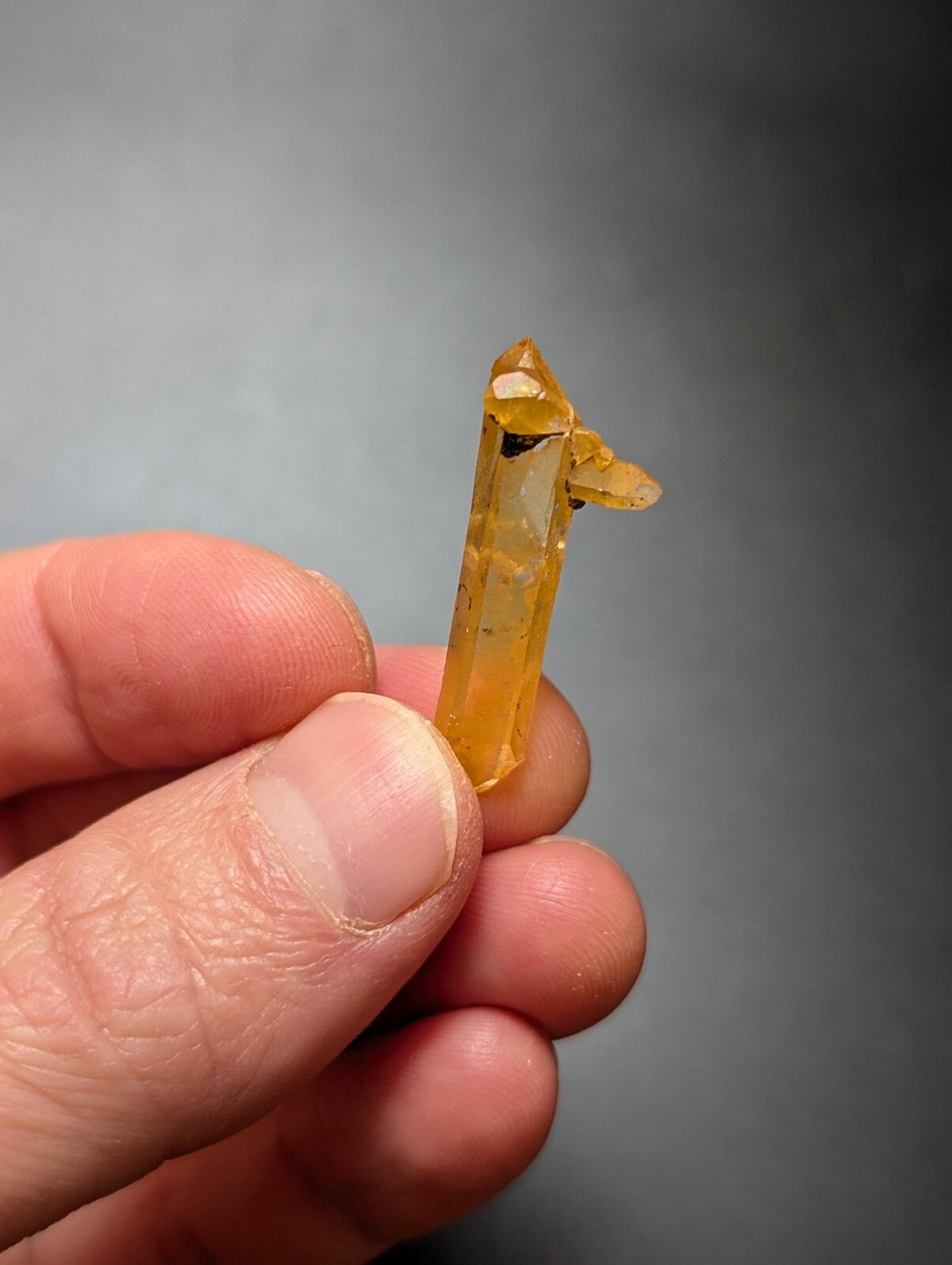 A translucent golden-yellow crystal with a pointed tip and natural facets, held gently between fingers.