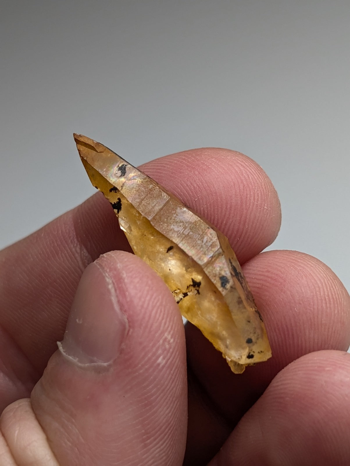 A translucent amber arkansas quartz crystal fragment with dark inclusions and a pointed tip from a set of 3