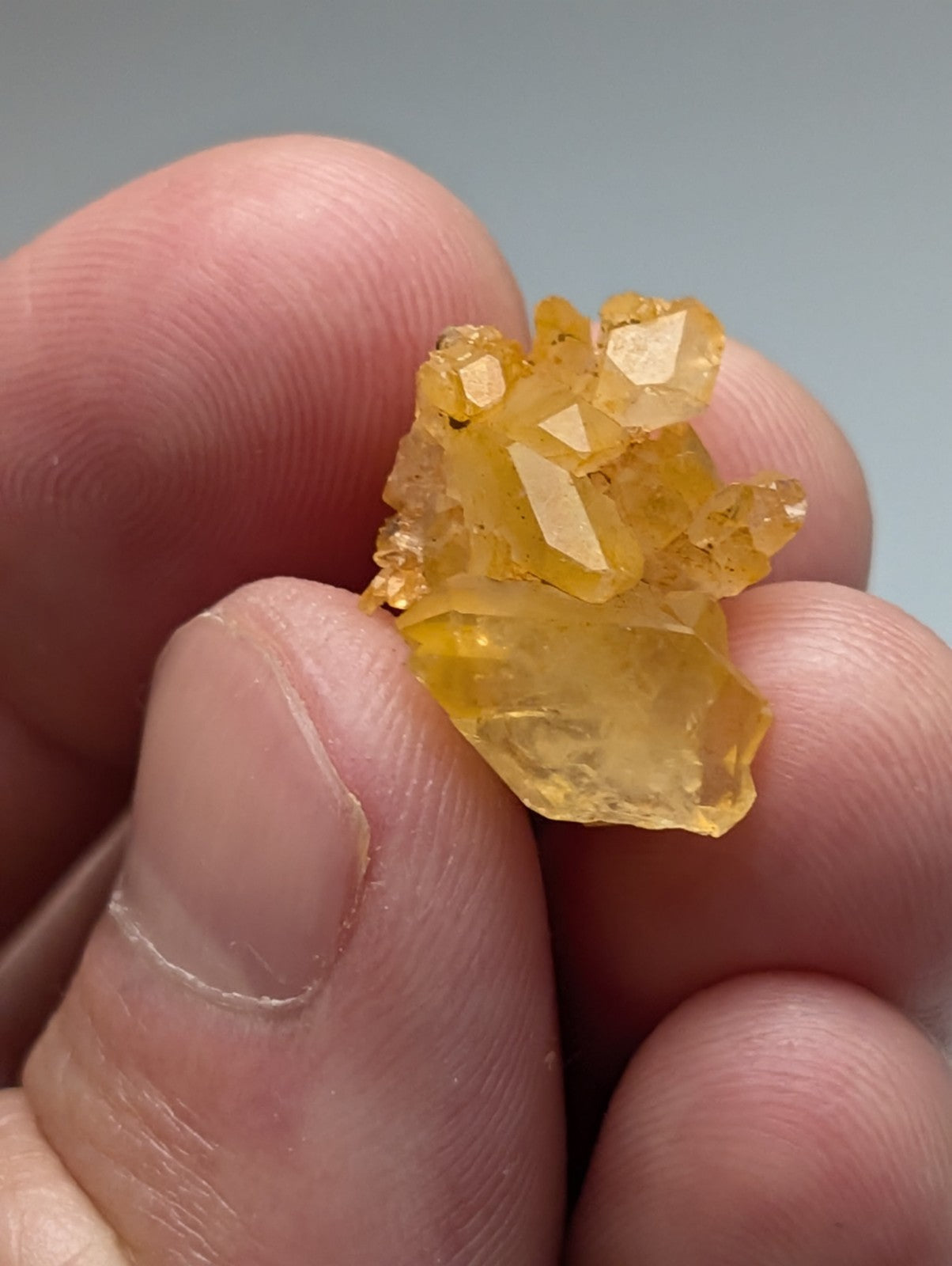 A cluster of translucent yellow Arkansas quartz crystals with natural iridescence held between fingers