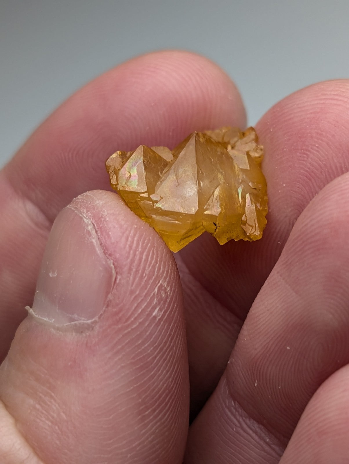 A translucent golden yellow arkansas quartz crystal with sharp angular facets and natural iridescence held in fingers