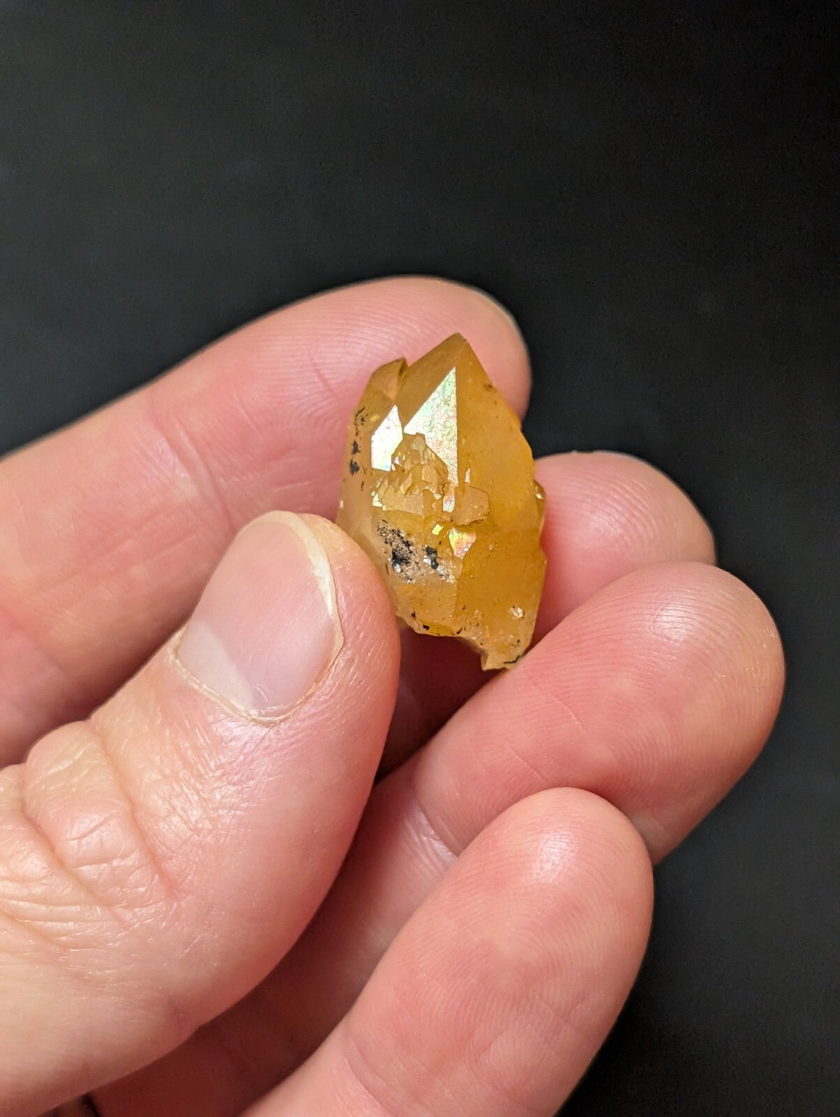 A translucent amber-colored crystal with a faceted, pointed tip and small dark inclusions.