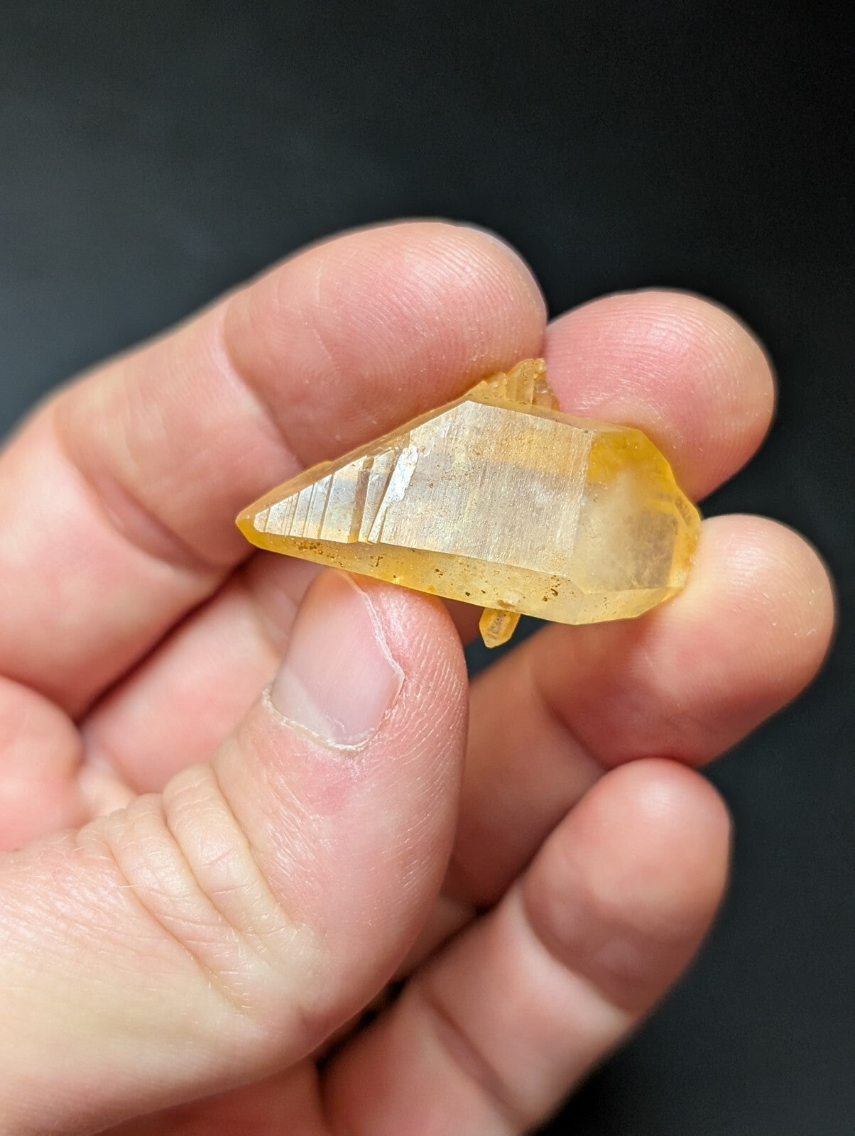 A translucent yellow crystal with a pointed, faceted tip and subtle internal striations.