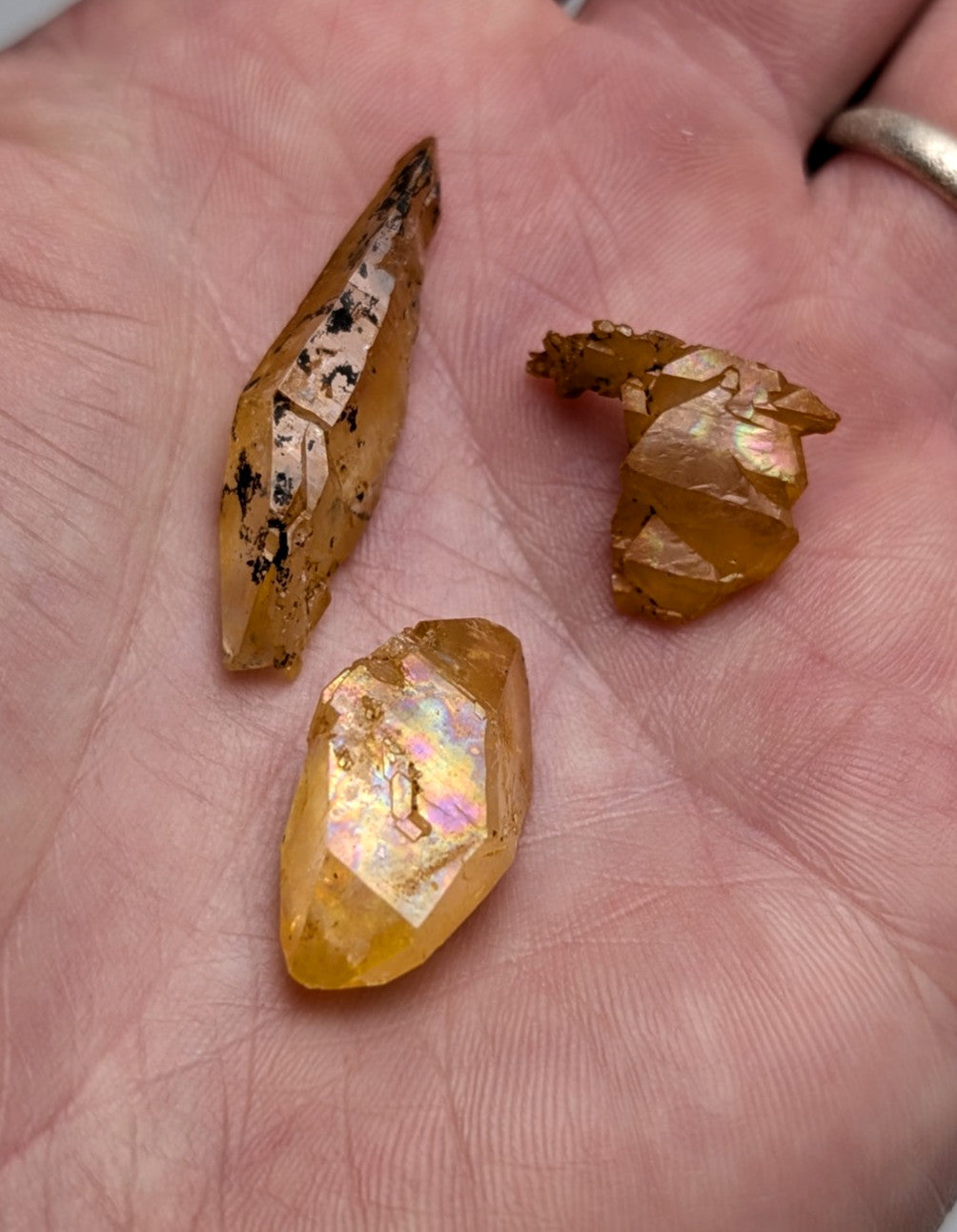 Set of 3 Arkansas quartz crystals with natural golden iridescence and rainbow flashes resting in an open palm