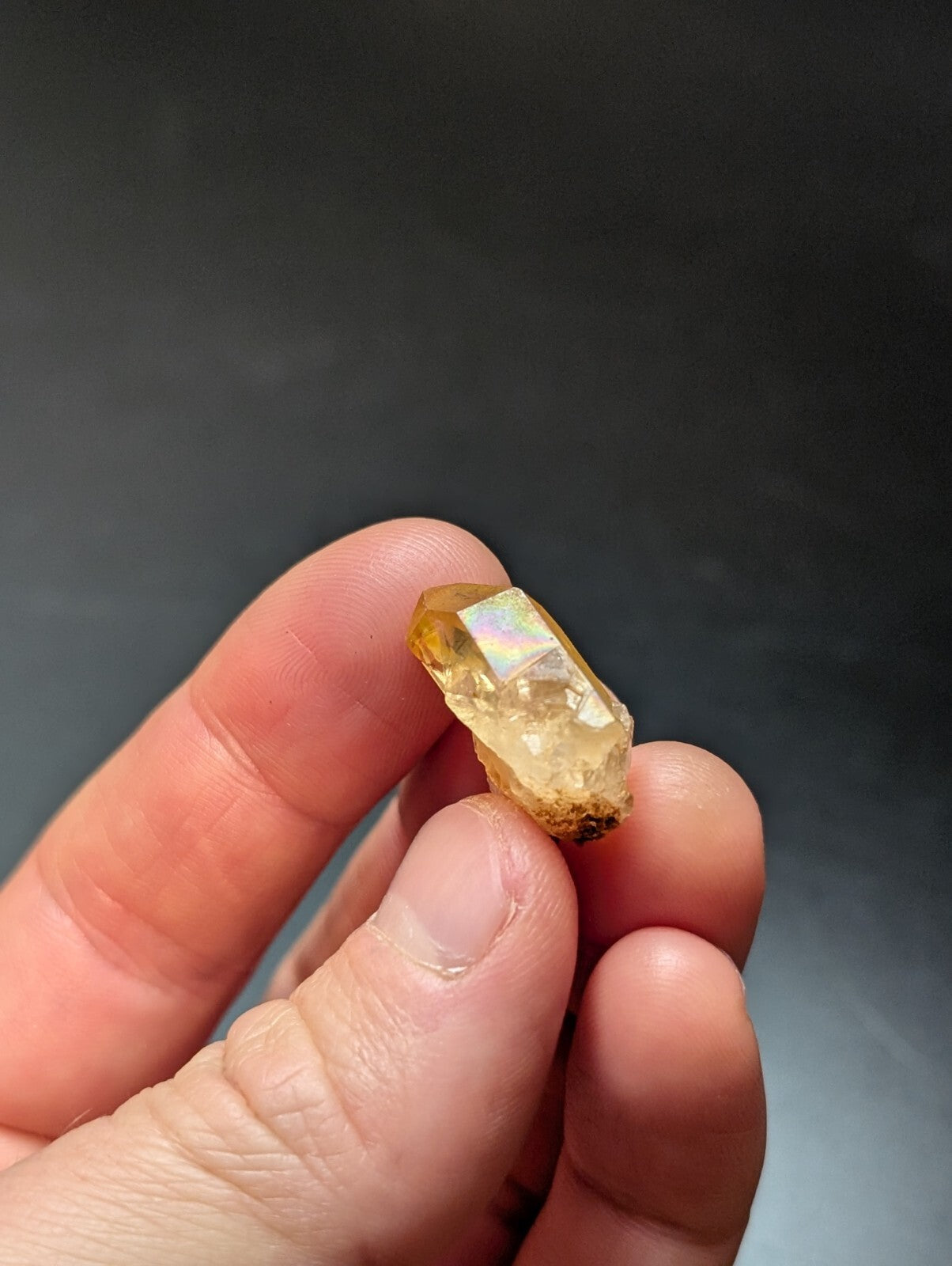 A translucent golden-yellow crystal with a faceted, iridescent surface held between fingers.