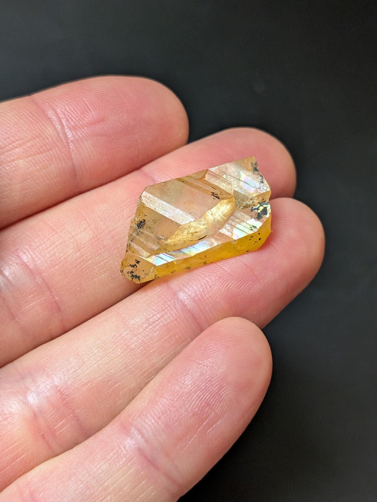 A translucent golden-yellow crystal with visible internal striations and dark inclusions, held gently in a person’s palm.