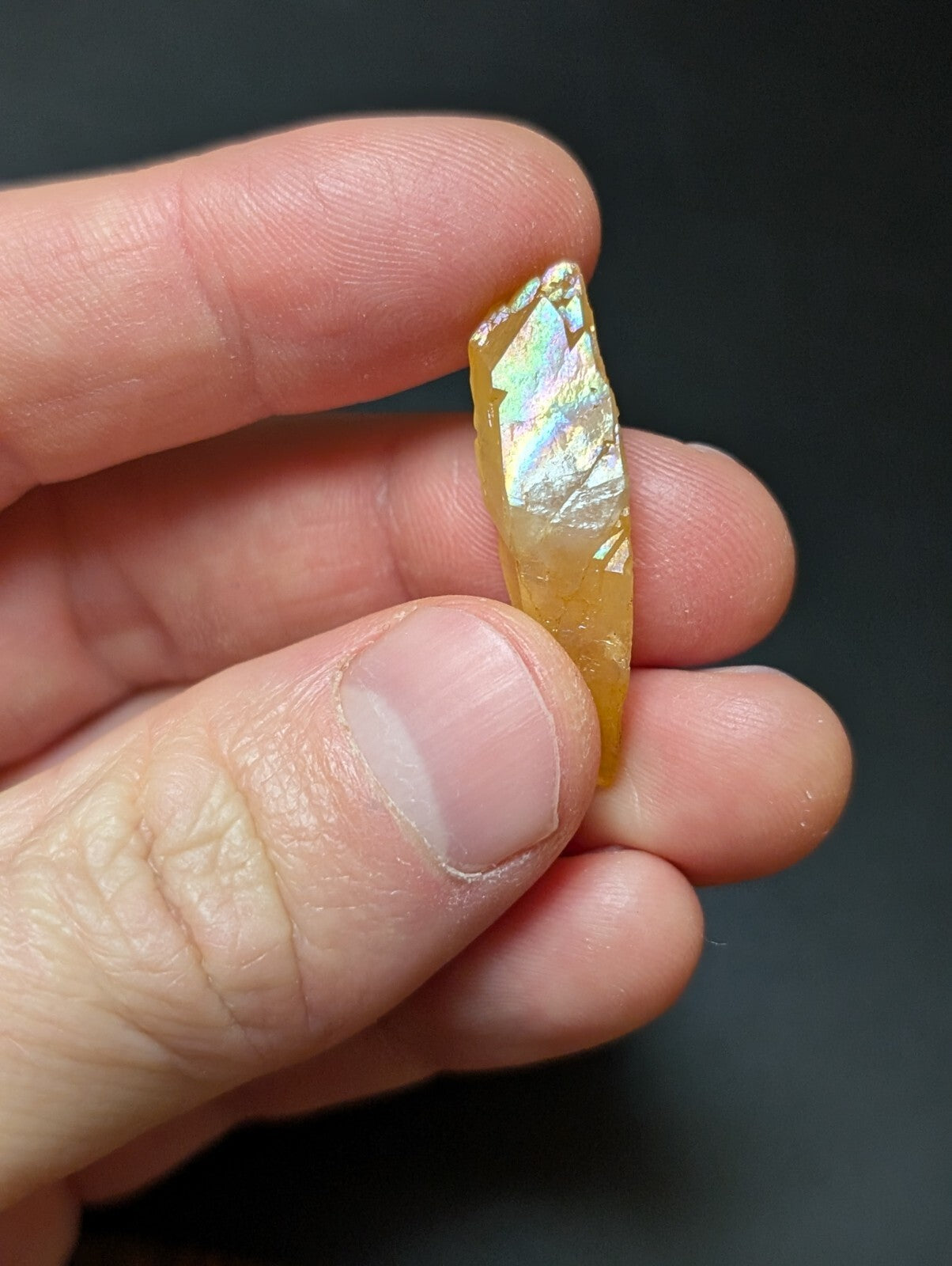A translucent golden-yellow opal with a shimmering, iridescent surface held delicately between fingers.