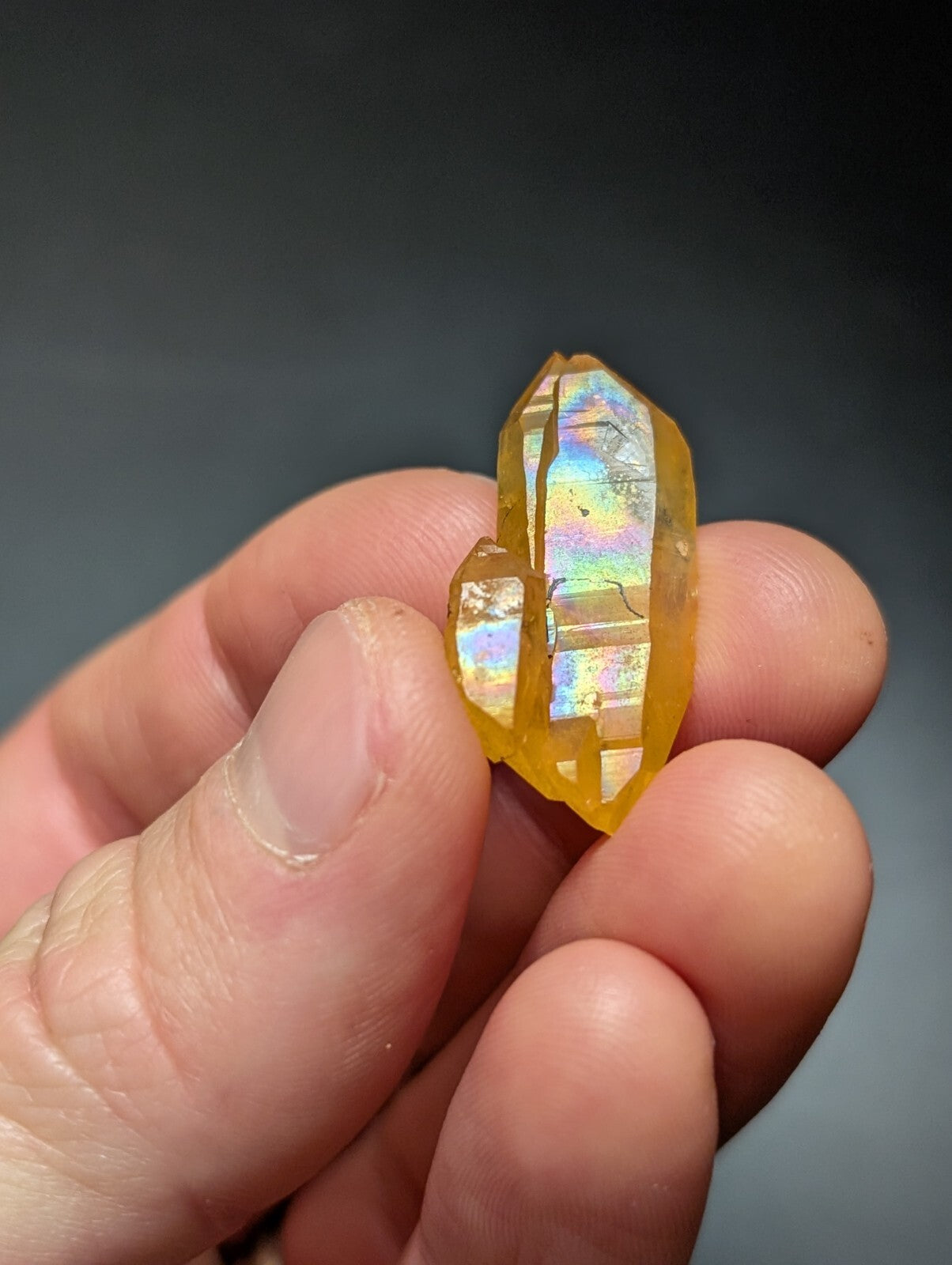 A translucent golden-yellow crystal with iridescent facets, held gently in a hand.