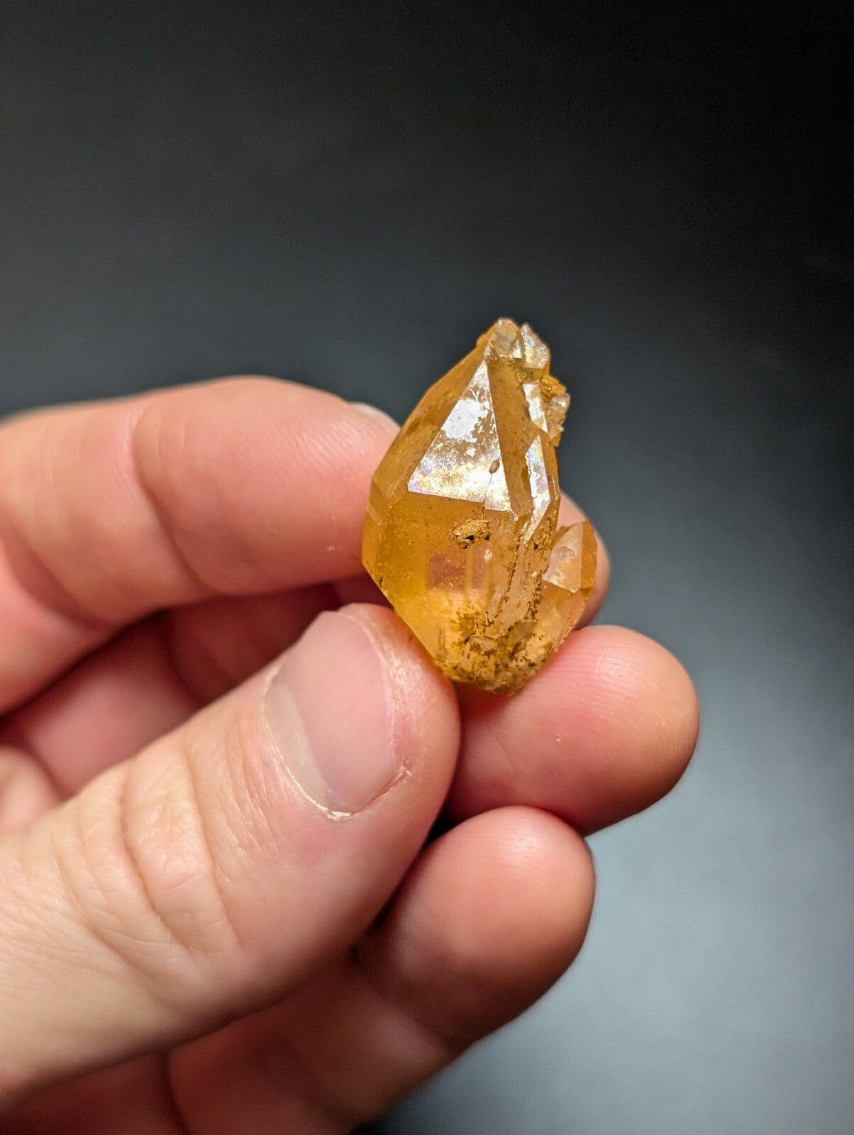 A translucent golden-yellow crystal with sharp, faceted edges and a slightly rough surface held gently in someone’s hand.