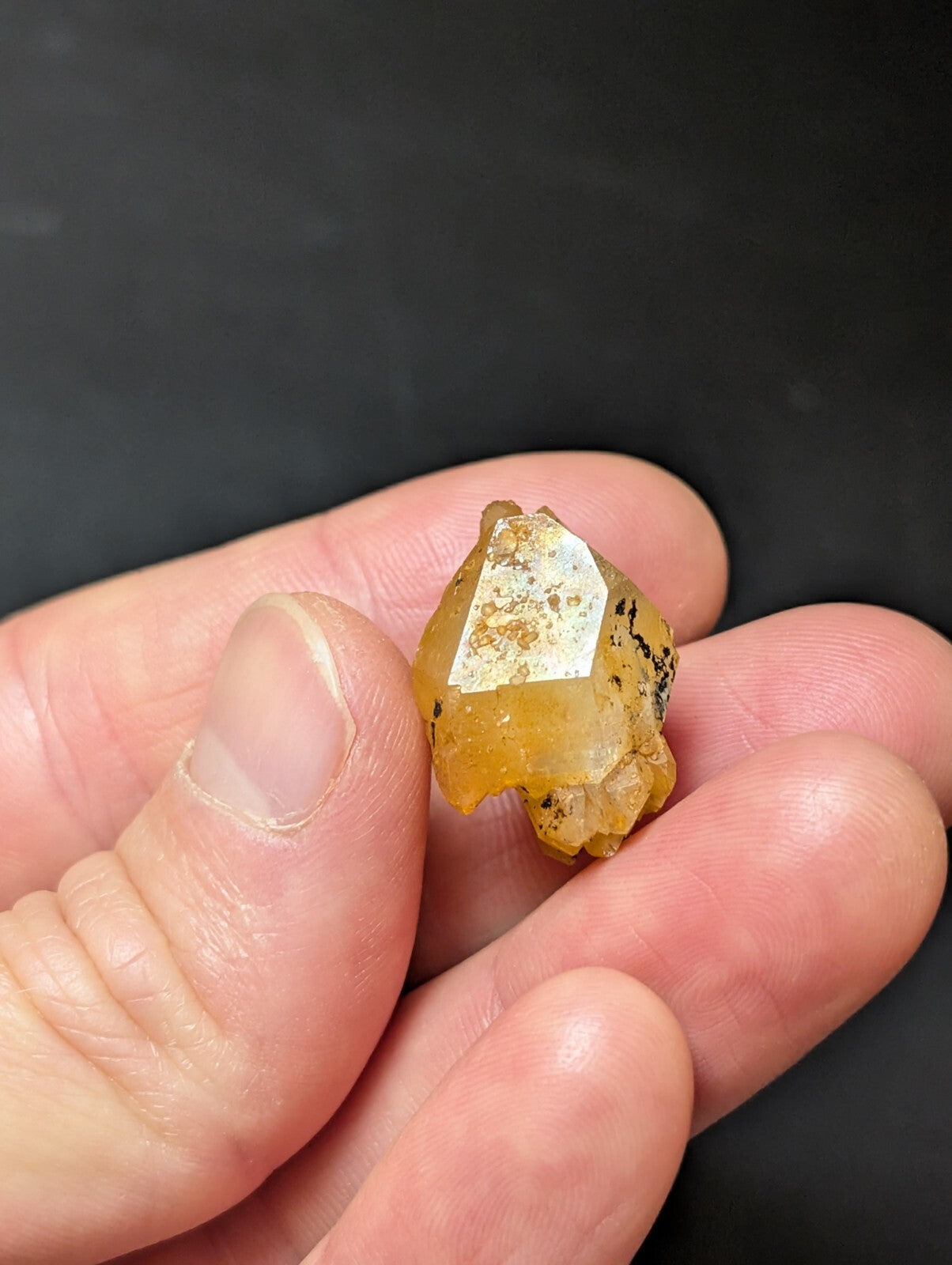 A translucent amber-colored crystal with a faceted, geometric shape and speckled inclusions.