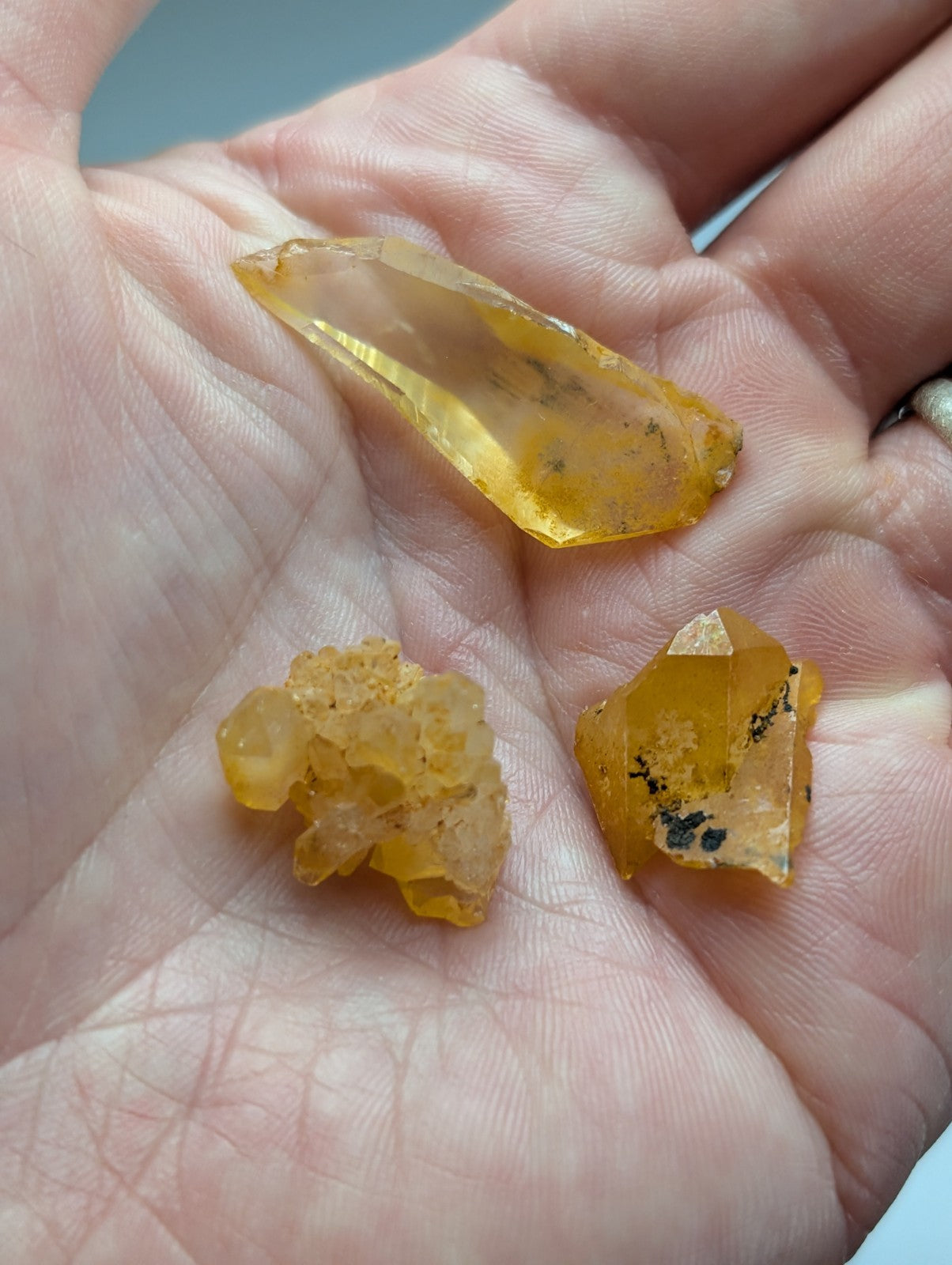 A hand holds a set of 3 yellow-orange Arkansas quartz crystals with natural iridescence and unique facets